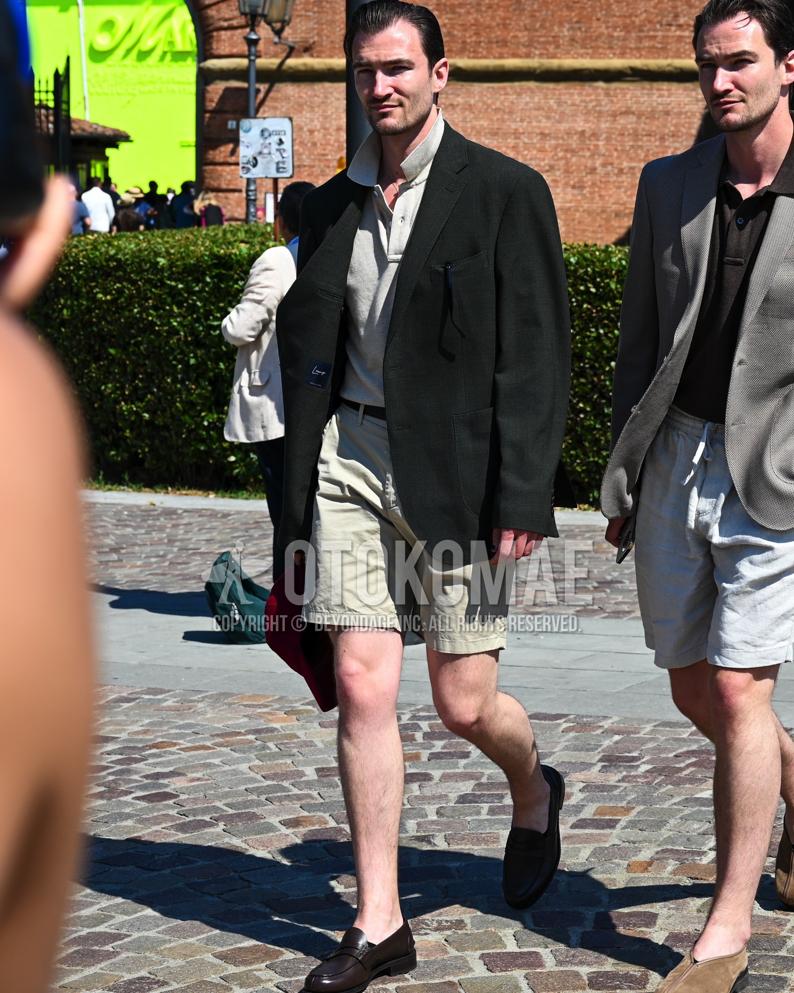Men's spring summer outfit with black plain tailored jacket, beige plain polo shirt, black plain leather belt, beige plain short pants, black  loafers leather shoes.