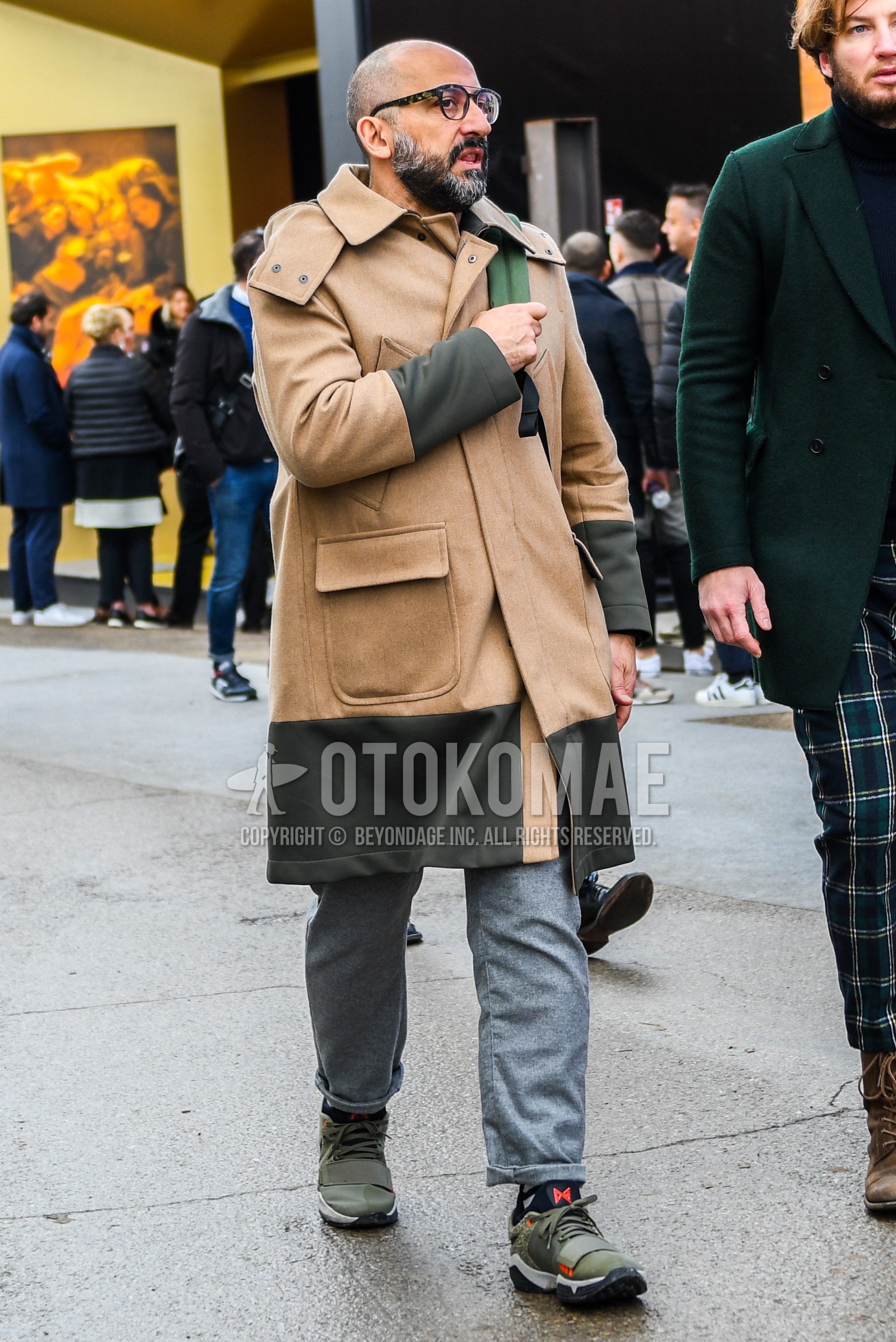Men's autumn winter outfit with plain glasses, beige plain outerwear, gray plain slacks, olive green low-cut sneakers.