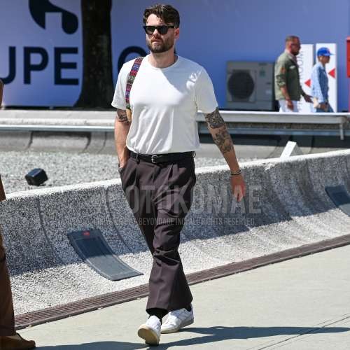 黒無地のサングラス、白無地のTシャツ、黒無地のレザーベルト、ブラウン無地のスラックス、ブラウン無地のプリーツパンツ、黒無地のソックス、白ローカットのスニーカー、マルチカラーバッグのトートバッグを合わせた夏春のメンズコーデ・着こなし。