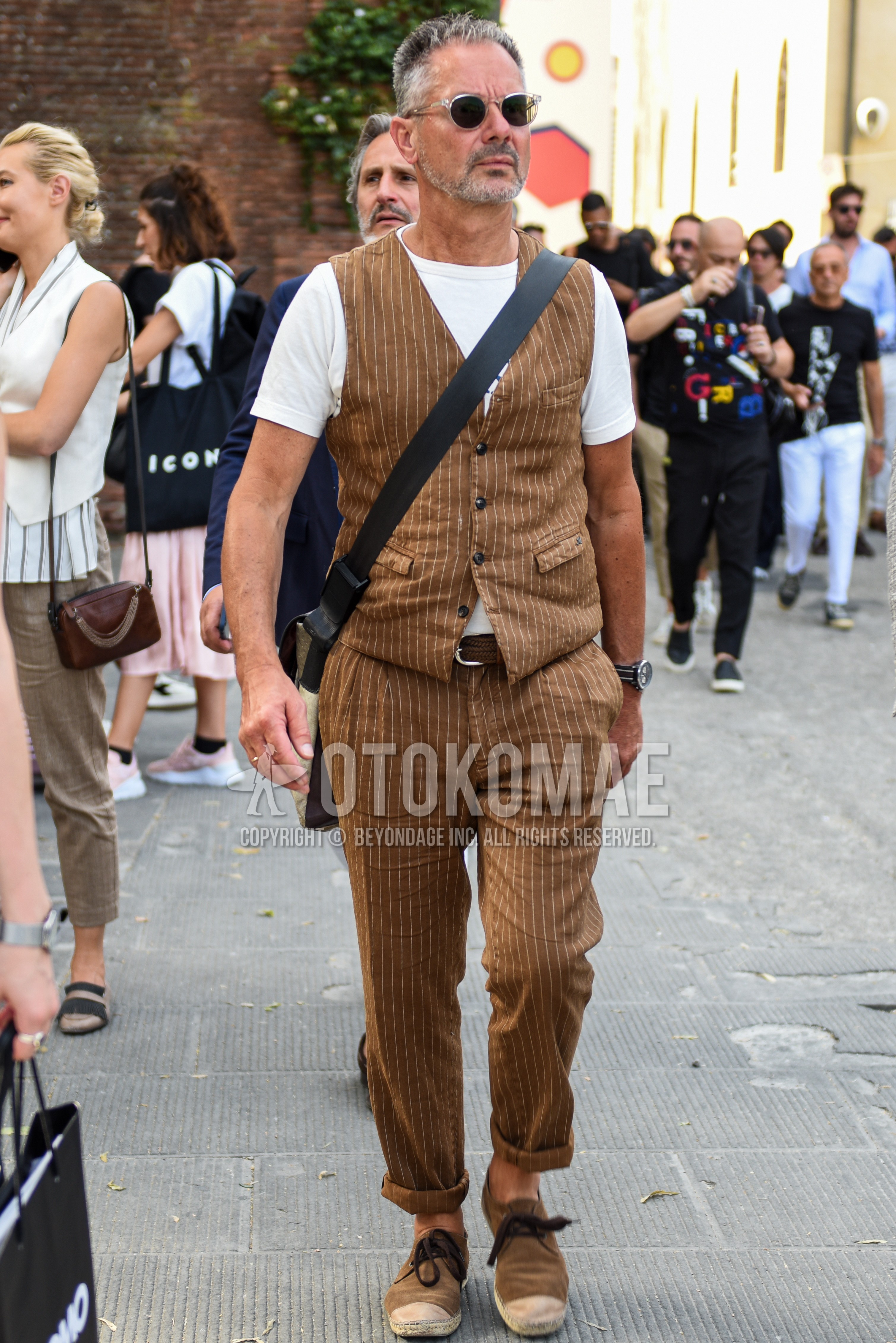 Men's spring summer outfit with clear plain sunglasses, white plain t-shirt, brown stripes gilet, brown plain leather belt, brown plain braided belt, brown stripes slacks, brown plain espadrille.