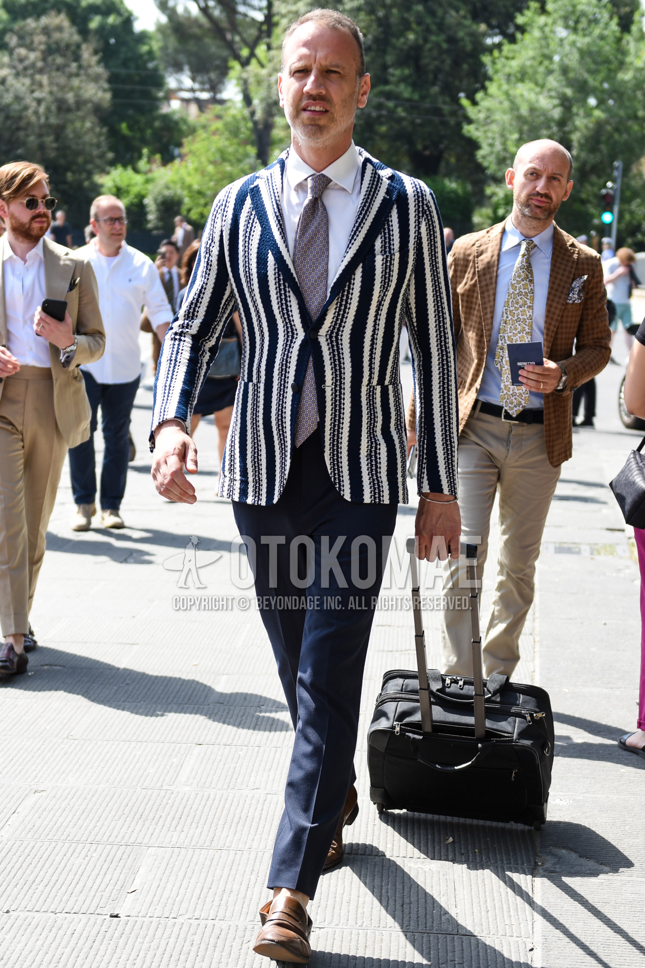 Men's spring summer autumn outfit with navy white stripes tailored jacket, white plain shirt, navy plain slacks, brown coin loafers leather shoes, gray necktie necktie.
