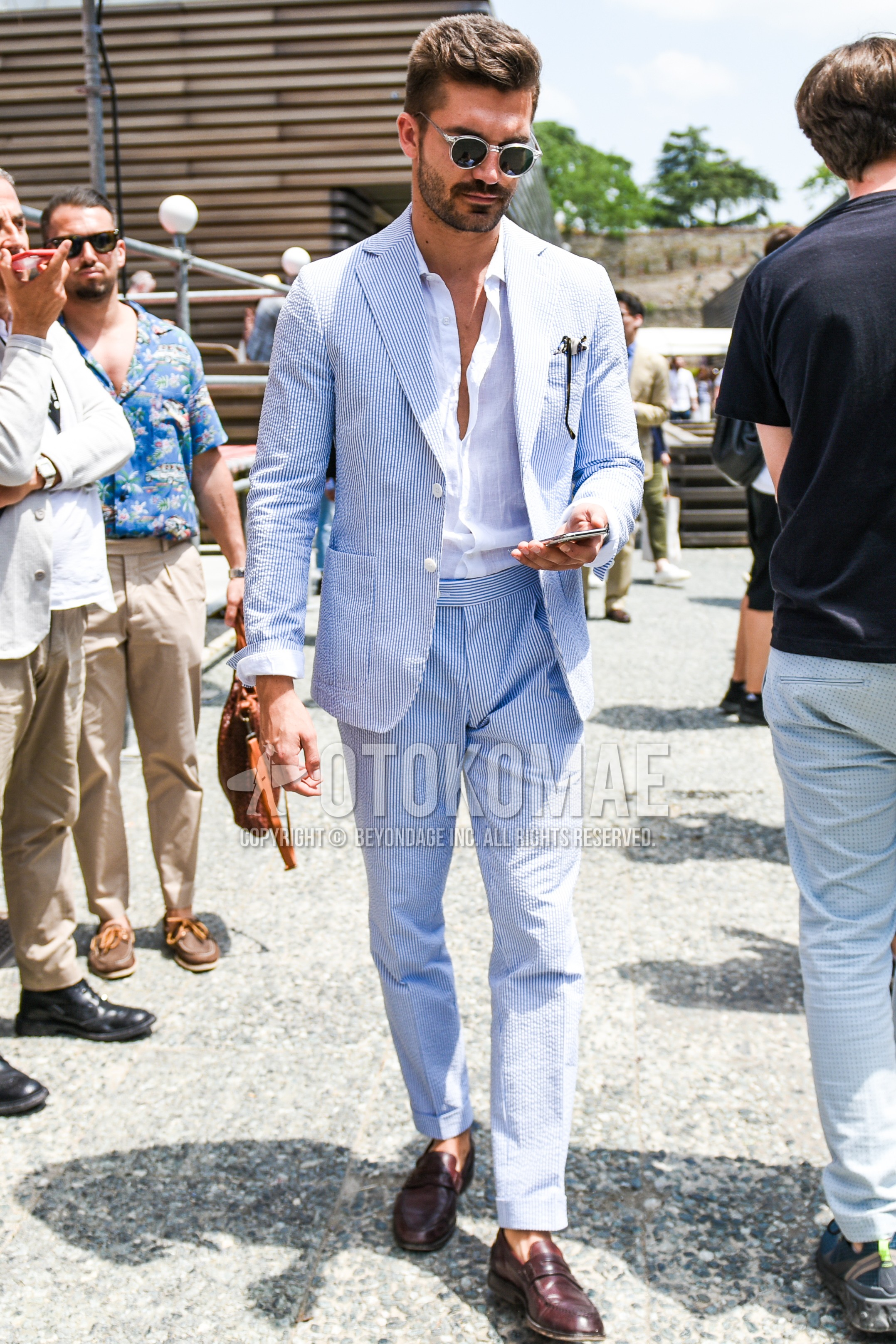 Men's summer outfit with clear plain sunglasses, white plain shirt, brown coin loafers leather shoes, light blue stripes suit.