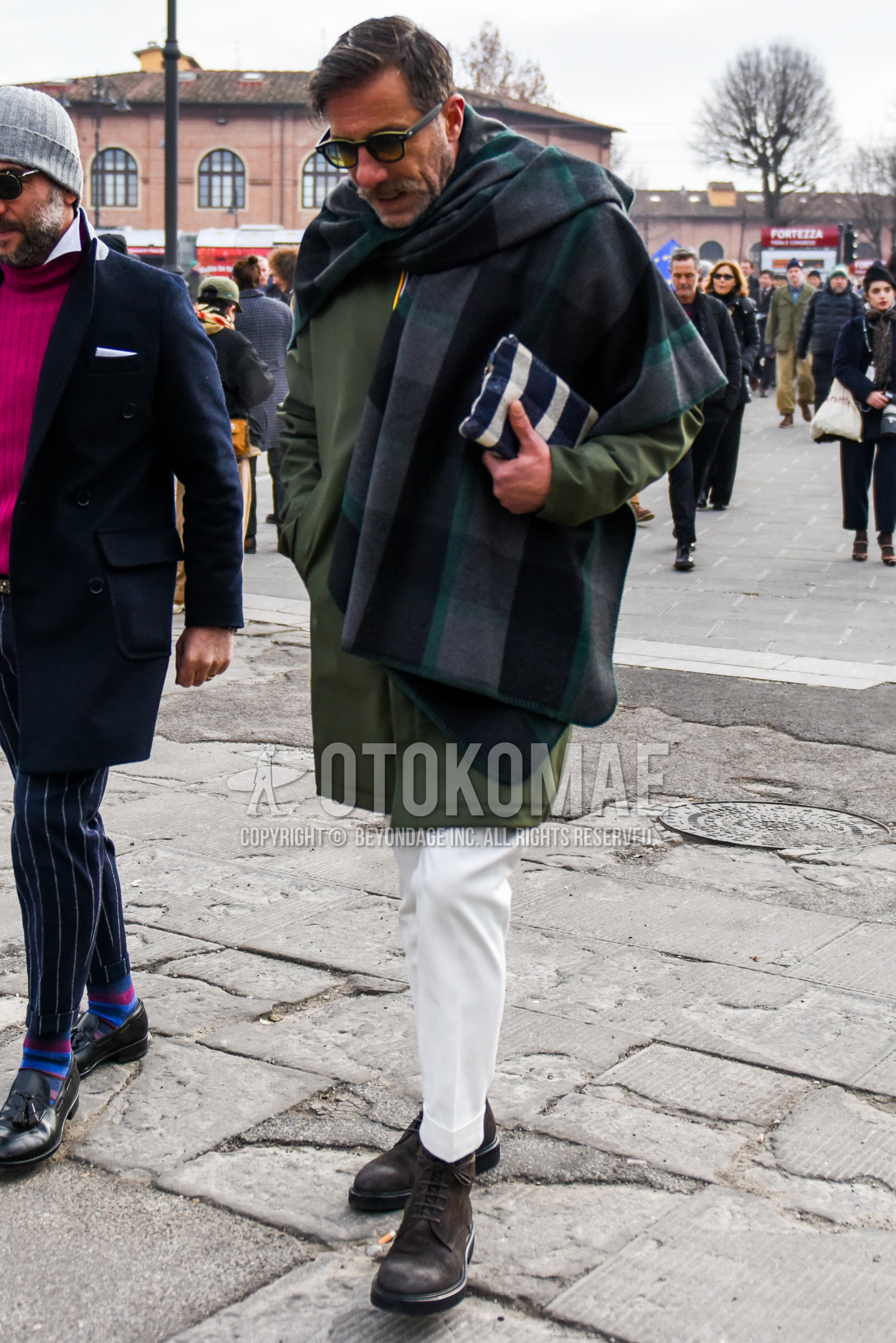 Men's autumn winter outfit with plain sunglasses, gray black check scarf, olive green plain stenkarrer coat, white plain slacks, brown  boots.