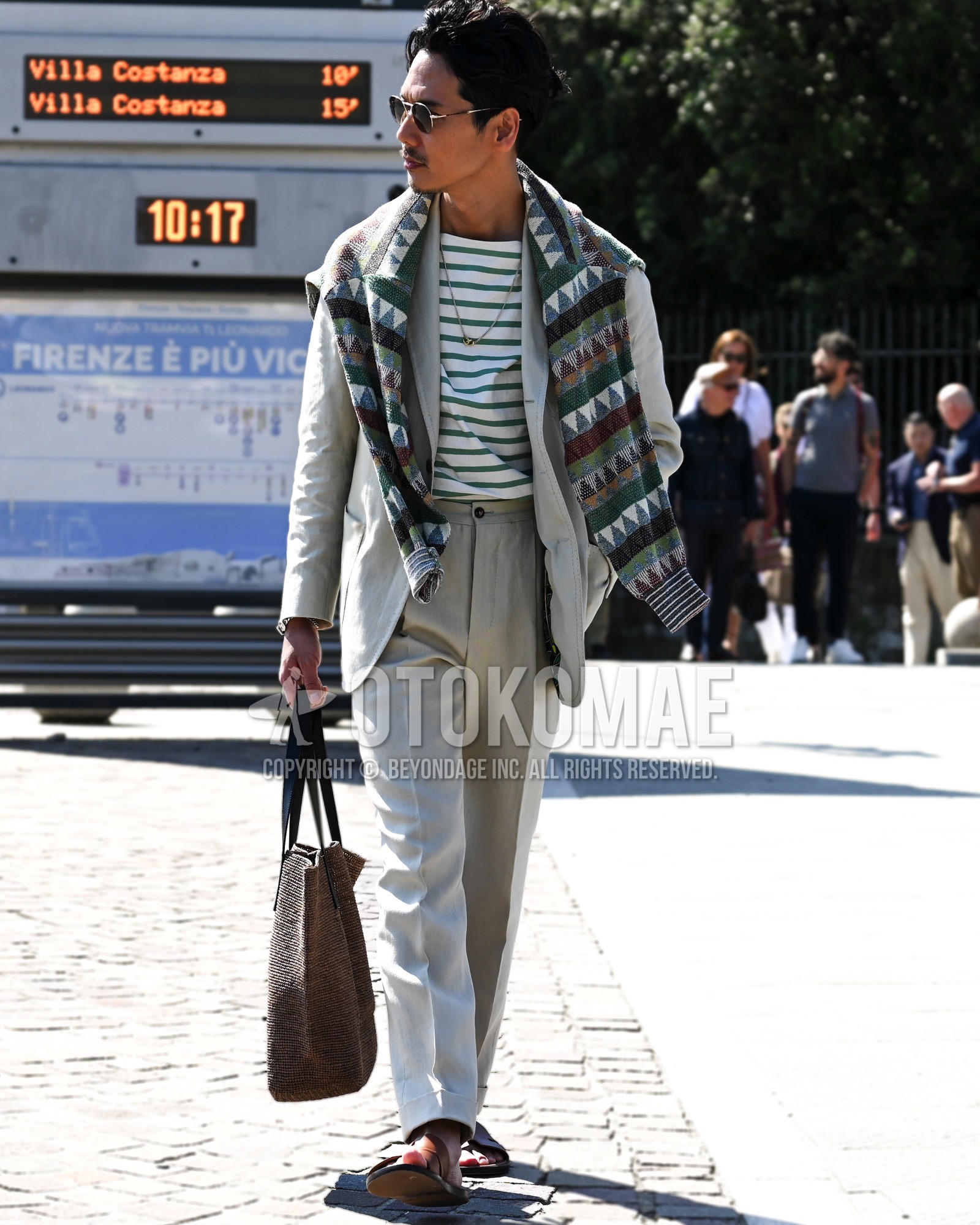 Men's spring summer autumn outfit with black plain sunglasses, green horizontal stripes t-shirt, green whole pattern sweater, brown leather sandals, brown plain tote bag, white plain suit.