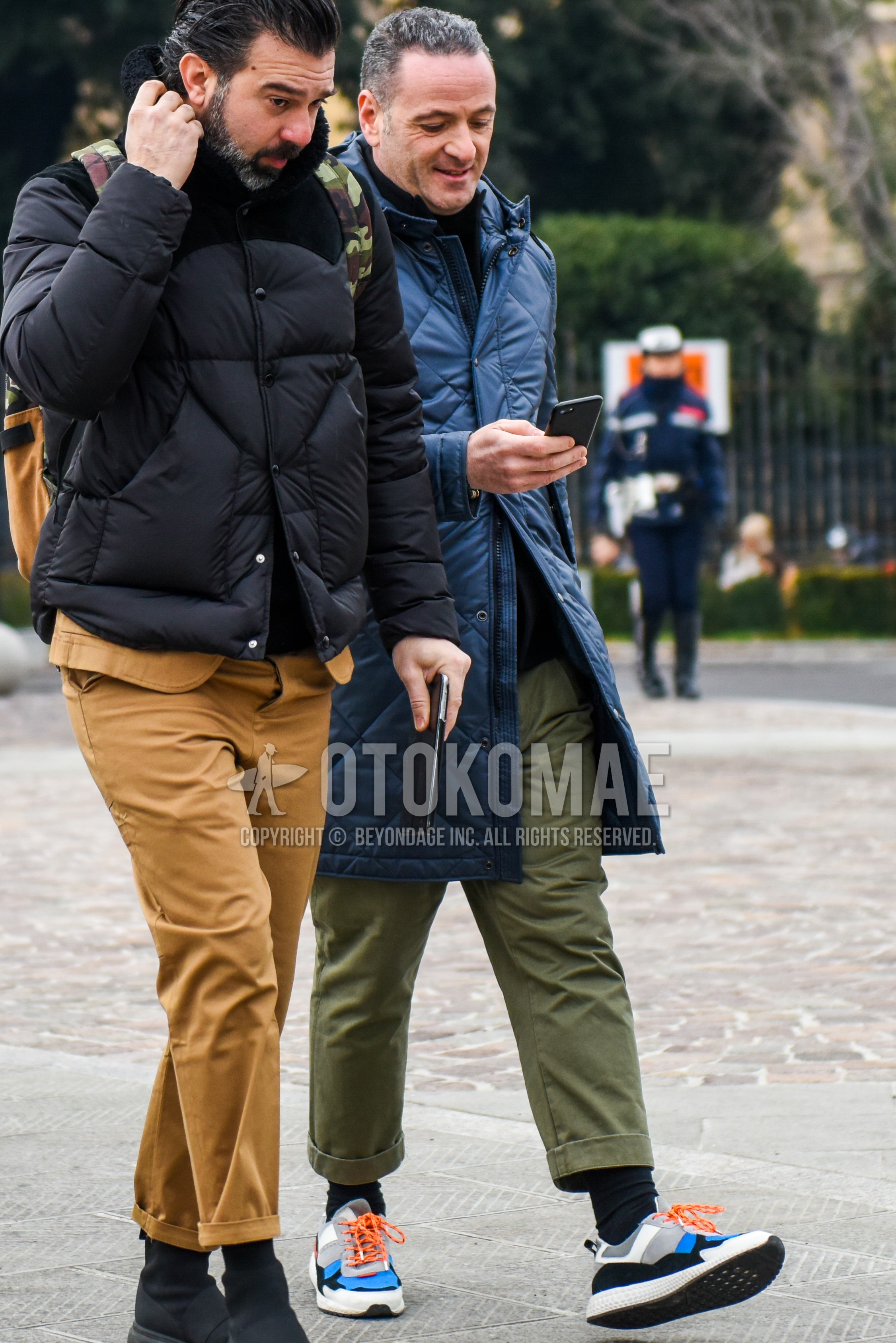 Men's autumn winter outfit with navy plain down jacket, olive green plain chinos, black plain socks, multi-color low-cut sneakers.