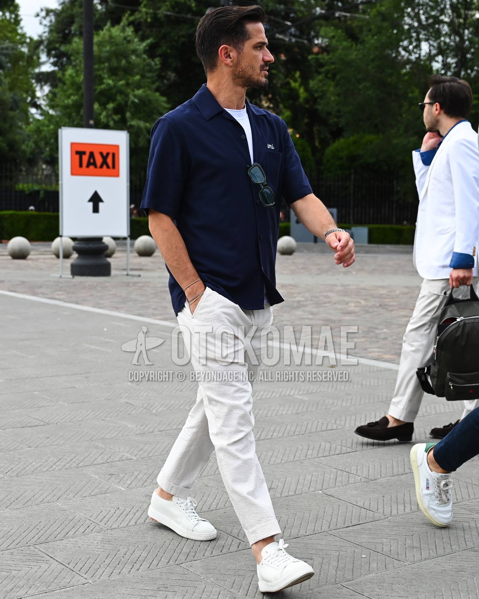 Men's spring summer outfit with navy plain shirt, white plain t-shirt, white plain slacks, white low-cut sneakers.
