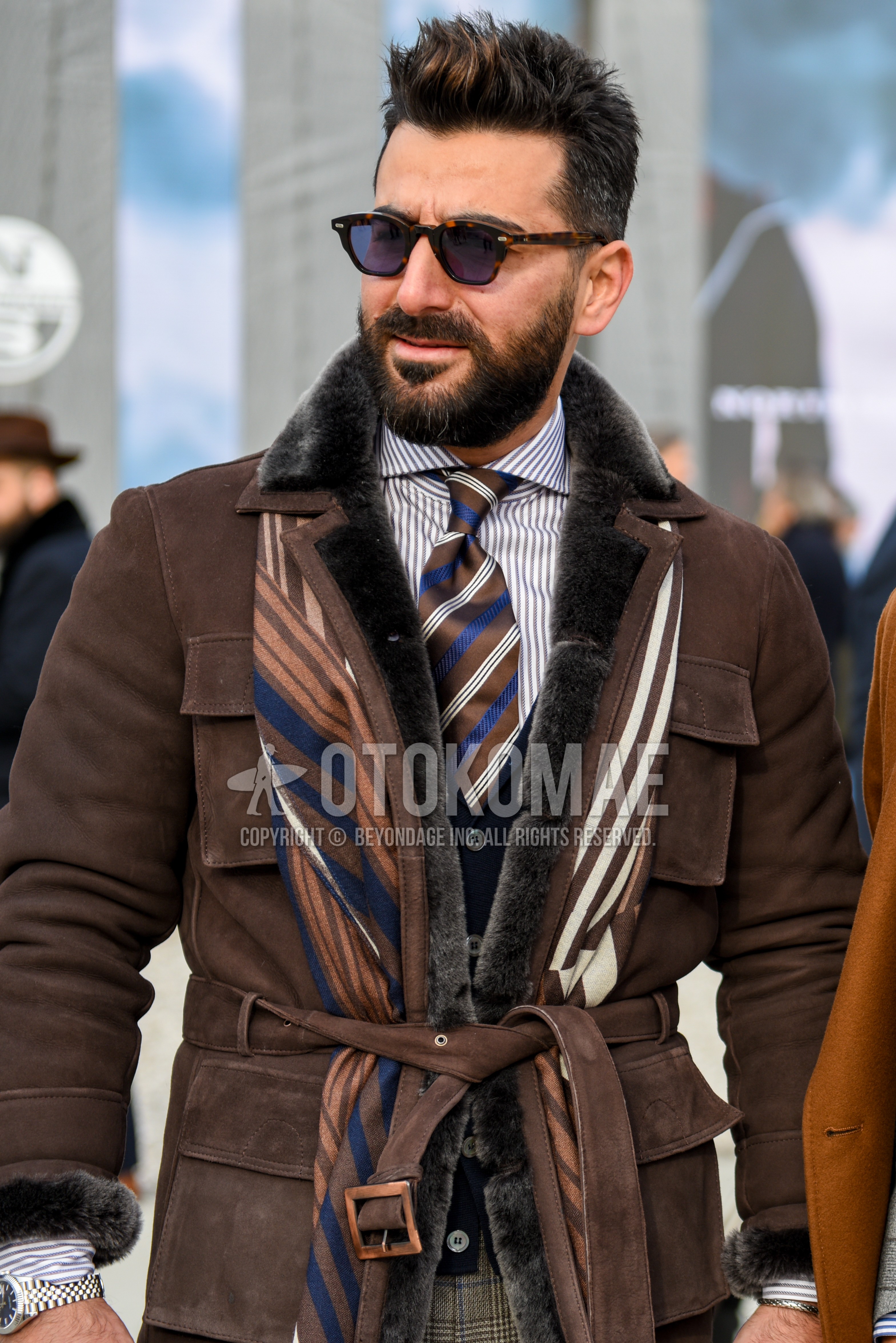 Men's autumn winter outfit with brown tortoiseshell sunglasses, multi-color scarf scarf, brown plain belted coat, white gray stripes shirt, black plain tailored jacket.
