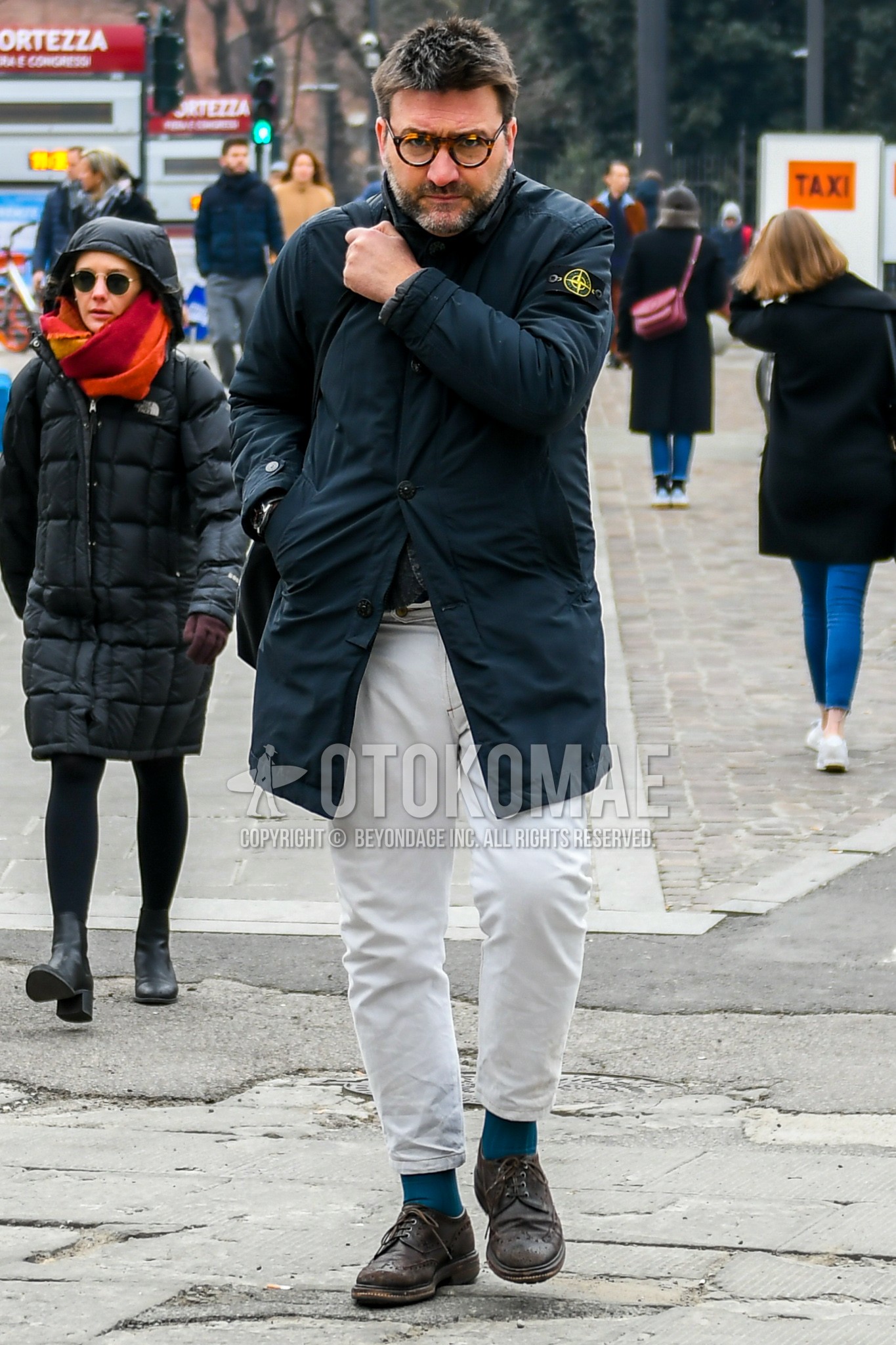 Men's winter outfit with brown tortoiseshell glasses, black plain stenkarrer coat, white plain cotton pants, white plain ankle pants, blue plain socks, brown wing-tip shoes leather shoes.
