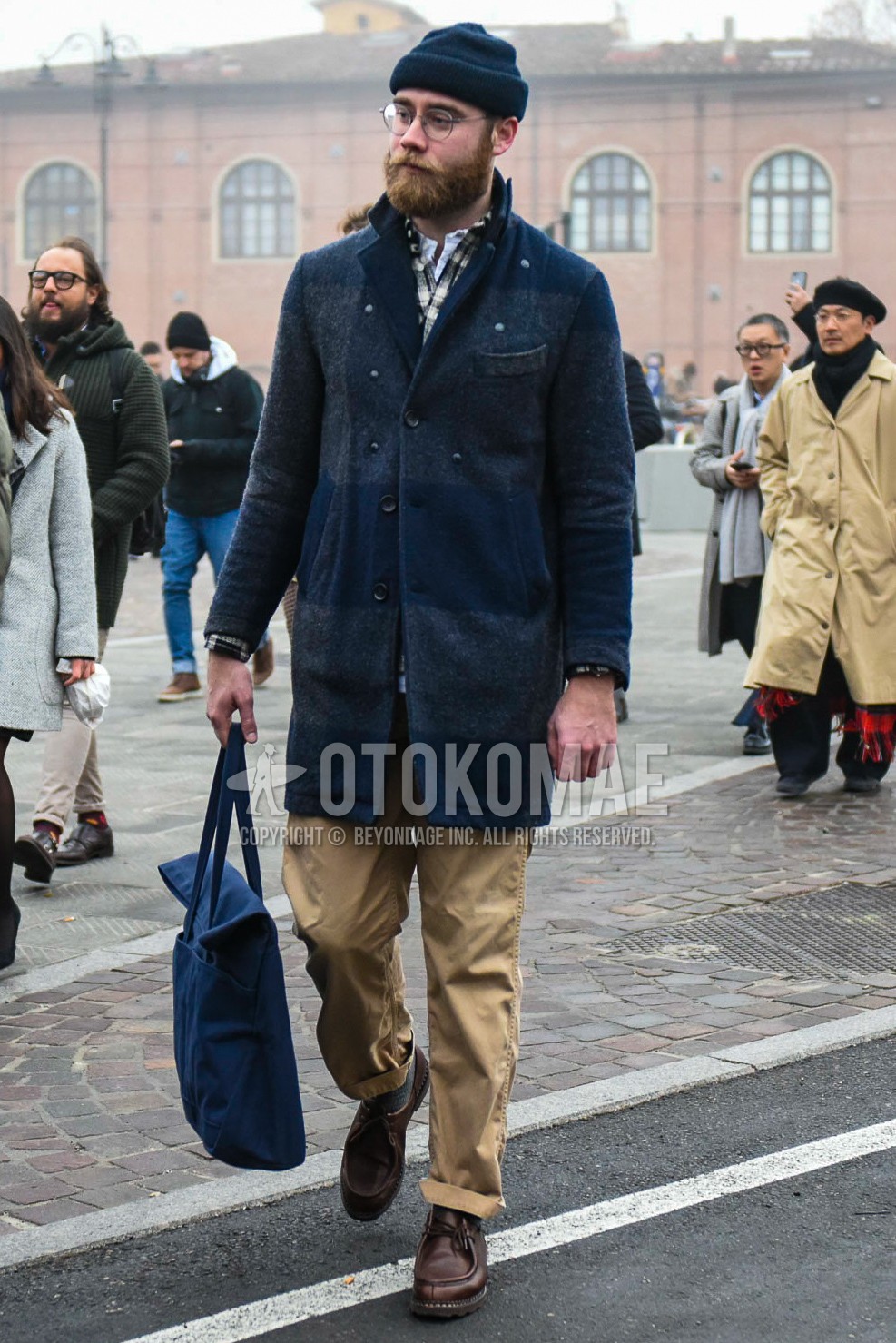 Men's winter outfit with plain glasses, navy horizontal stripes chester coat, beige plain chinos, brown  leather shoes, navy plain tote bag.