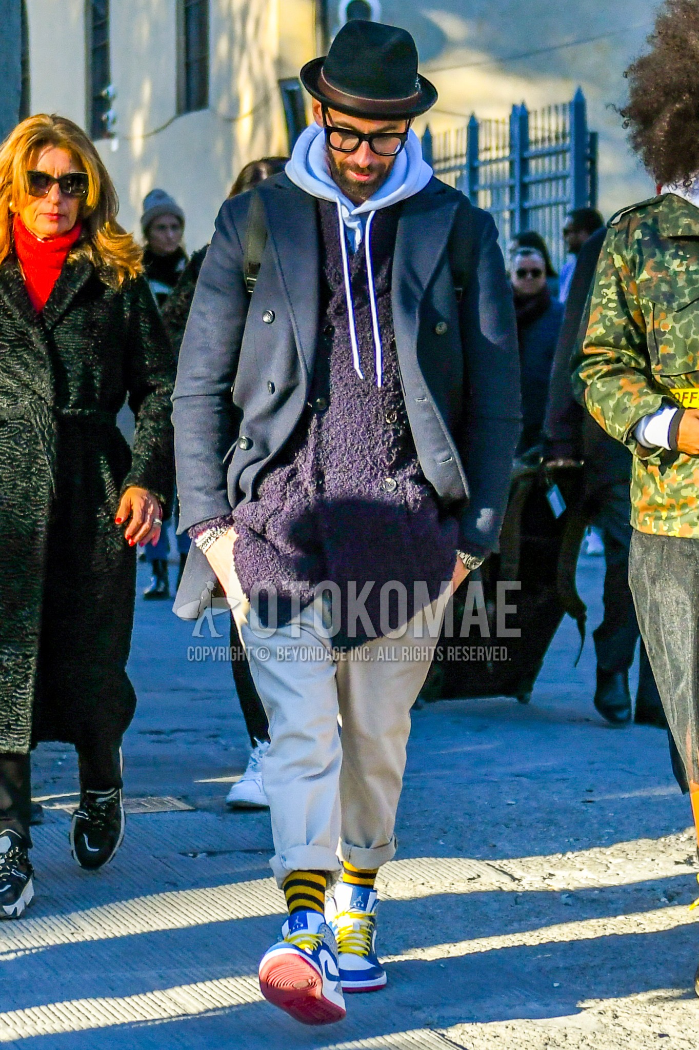 Men's winter outfit with navy plain hat, navy plain chester coat, purple plain outerwear, white plain hoodie, white plain cotton pants, yellow horizontal stripes socks, white high-cut sneakers.