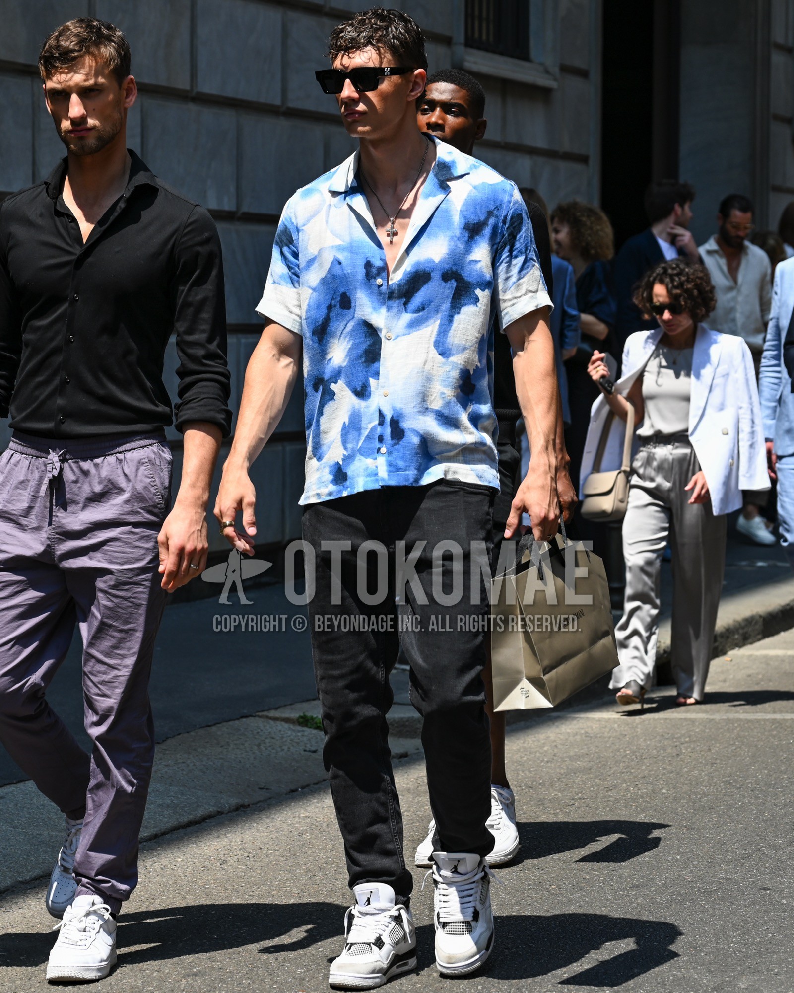 Men's spring summer outfit with black plain sunglasses, light blue whole pattern shirt, black plain chinos, white high-cut sneakers.