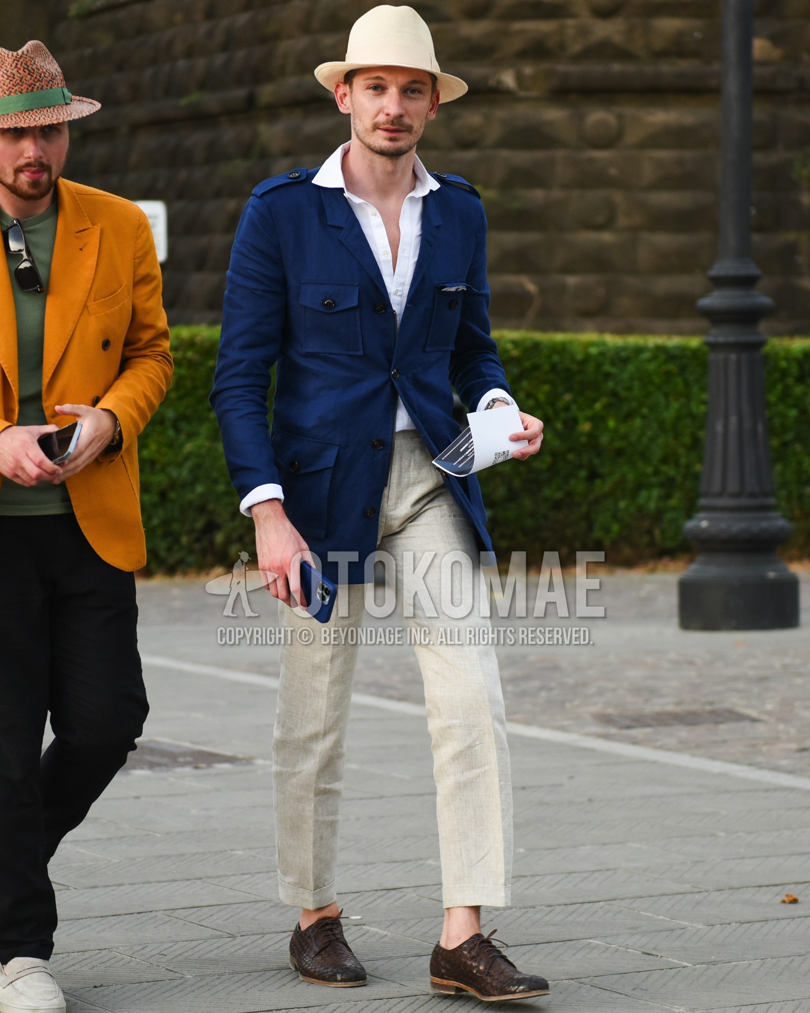 Men's spring summer outfit with beige plain hat, navy plain safari jacket, white plain shirt, beige plain slacks, brown plain toe leather shoes.