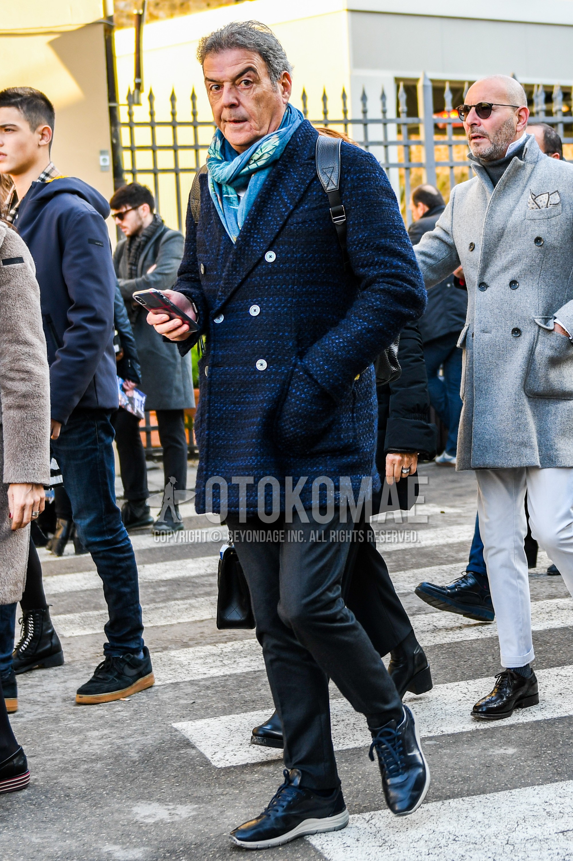 Men's winter outfit with light blue plain scarf, navy plain chester coat, dark gray plain slacks, black low-cut sneakers.