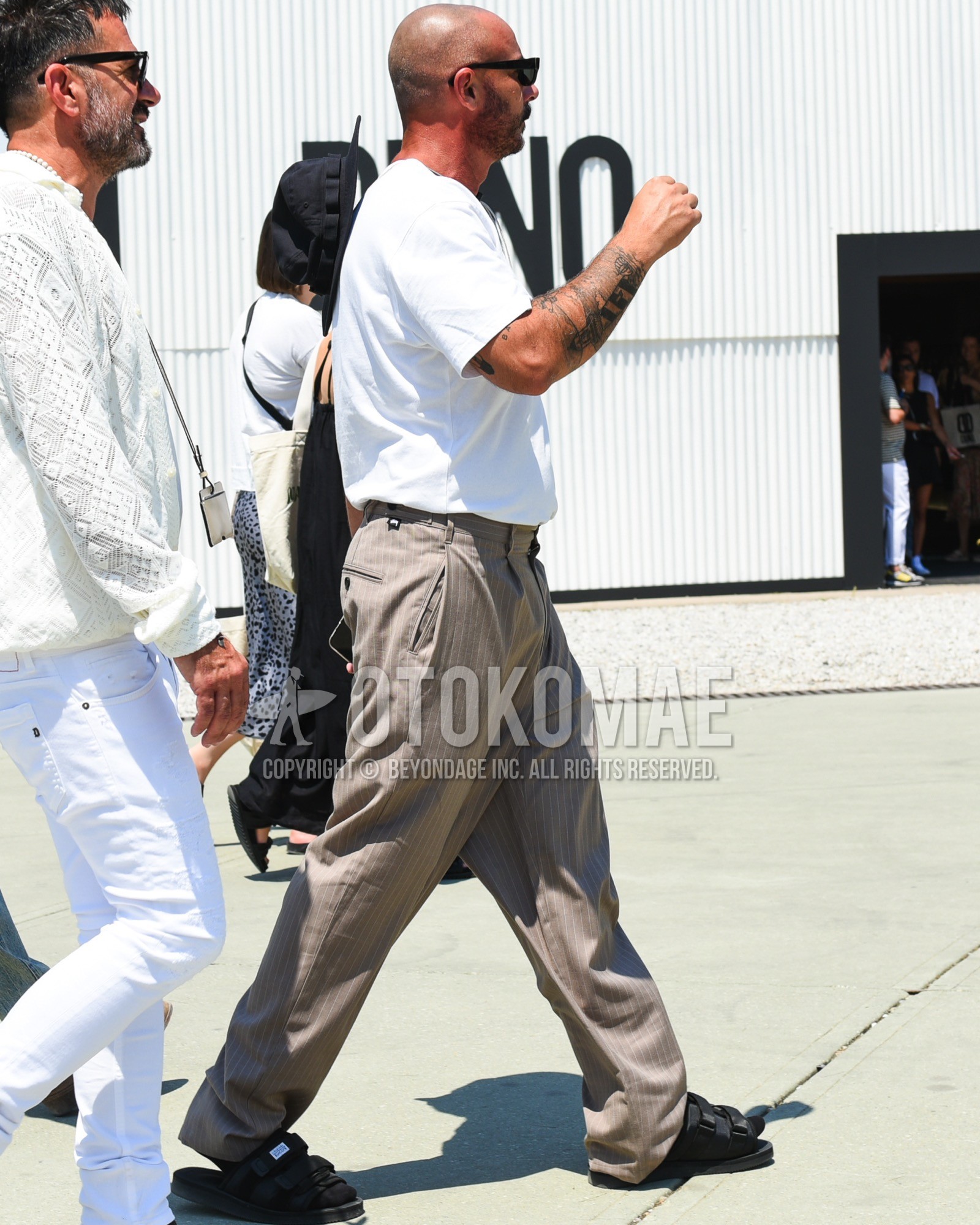 Men's spring summer outfit with black plain sunglasses, white plain t-shirt, beige stripes slacks, black plain socks, black sport sandals.