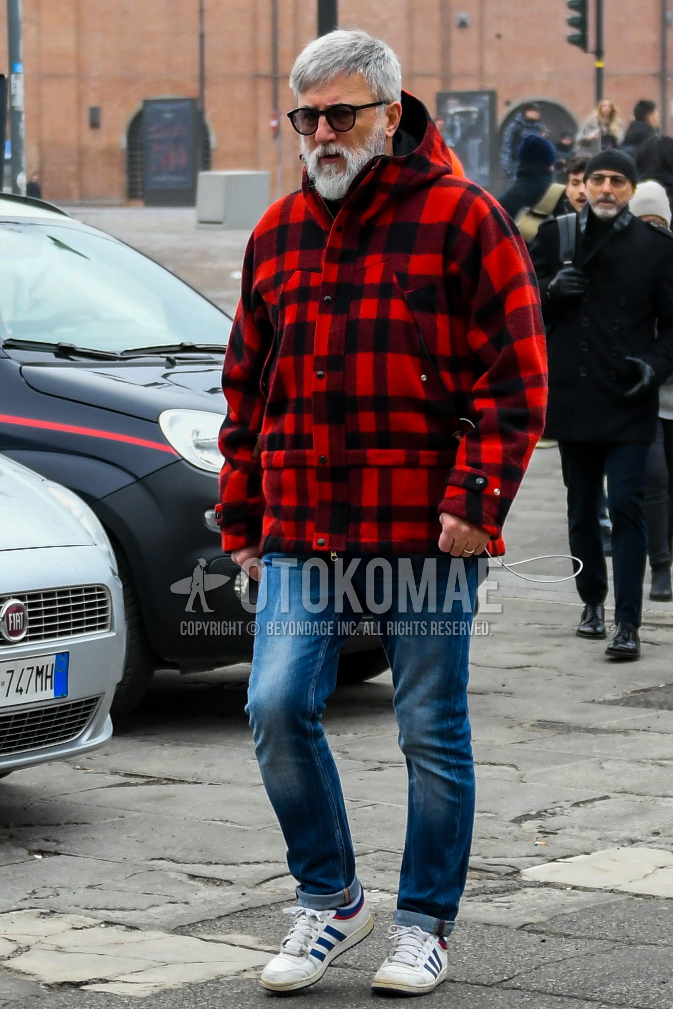Men's winter outfit with plain sunglasses, black red check down jacket, blue plain denim/jeans, white low-cut sneakers.