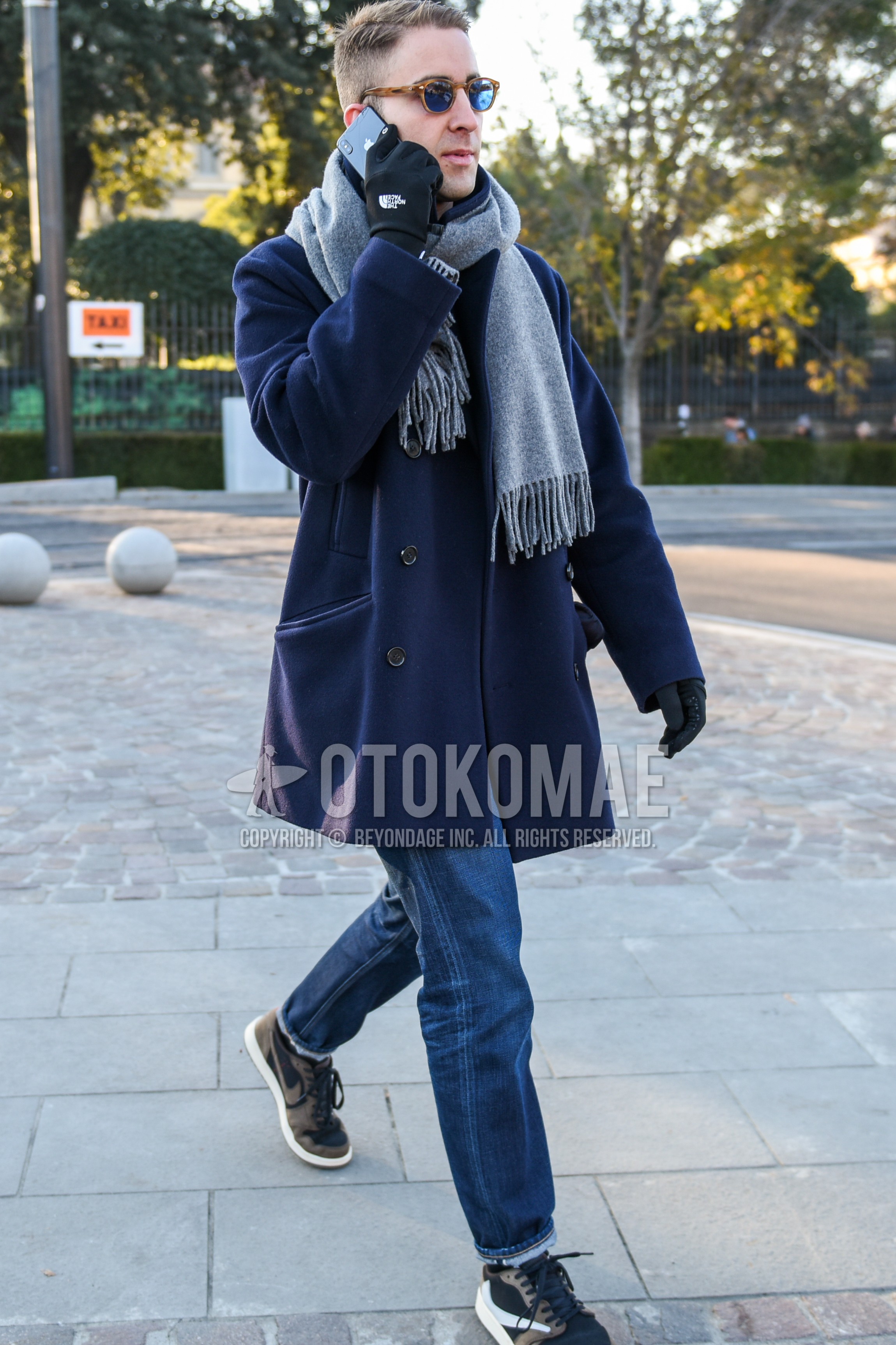 Men's autumn winter outfit with beige tortoiseshell sunglasses, gray plain scarf, navy plain p coat, blue plain denim/jeans, brown low-cut sneakers.