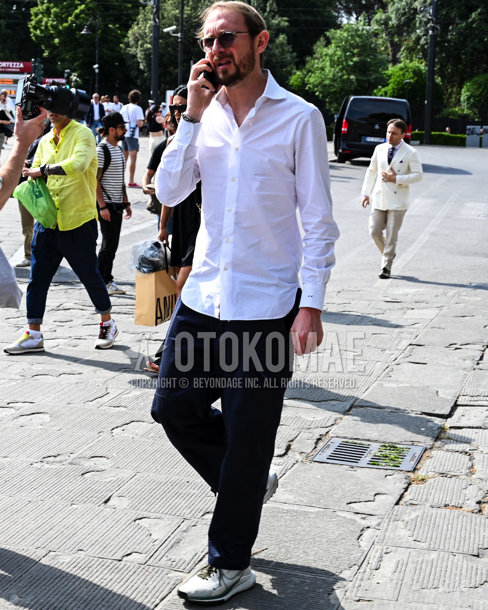 Men's spring summer autumn outfit with white plain shirt, navy plain chinos, white low-cut sneakers.