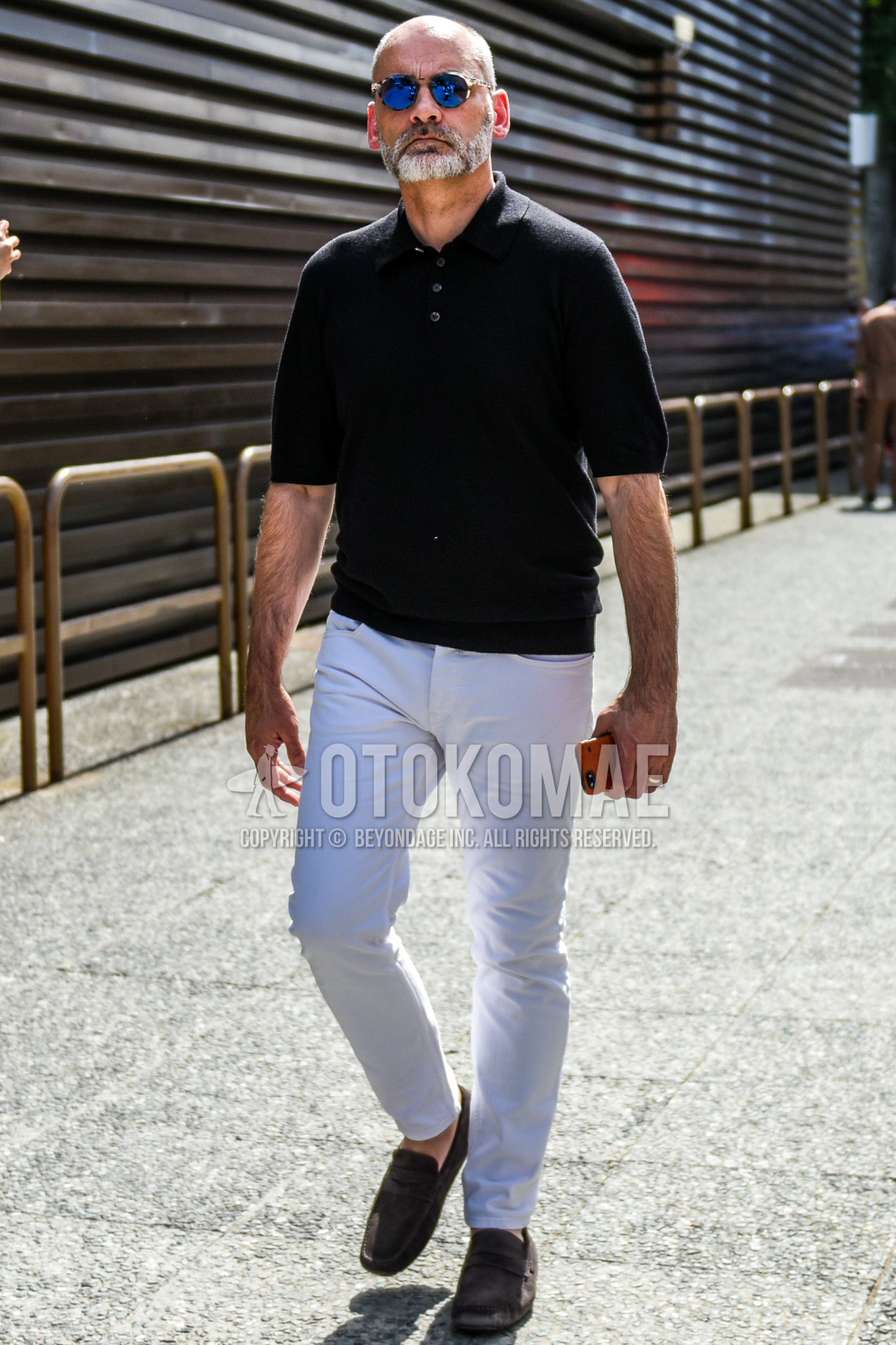 Men's spring summer outfit with clear tortoiseshell sunglasses, black plain polo shirt, white plain denim/jeans, brown coin loafers leather shoes.
