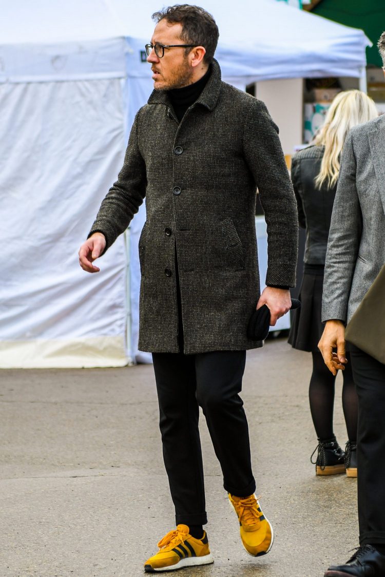Black turtleneck knit and black trousers accentuate the presence of the leading coat.