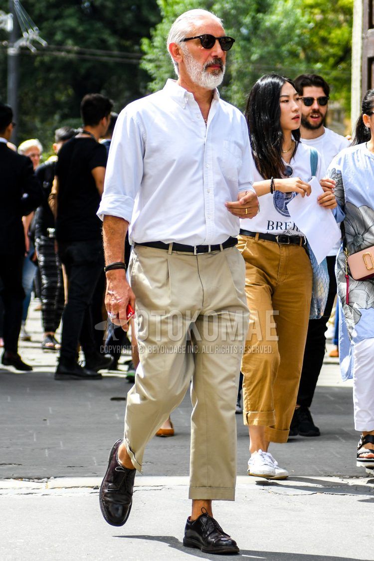 Spring, summer and fall men's coordinate outfit with brown tortoiseshell sunglasses, plain white shirt, plain black leather belt, plain beige slacks and black plain-toe leather shoes.
