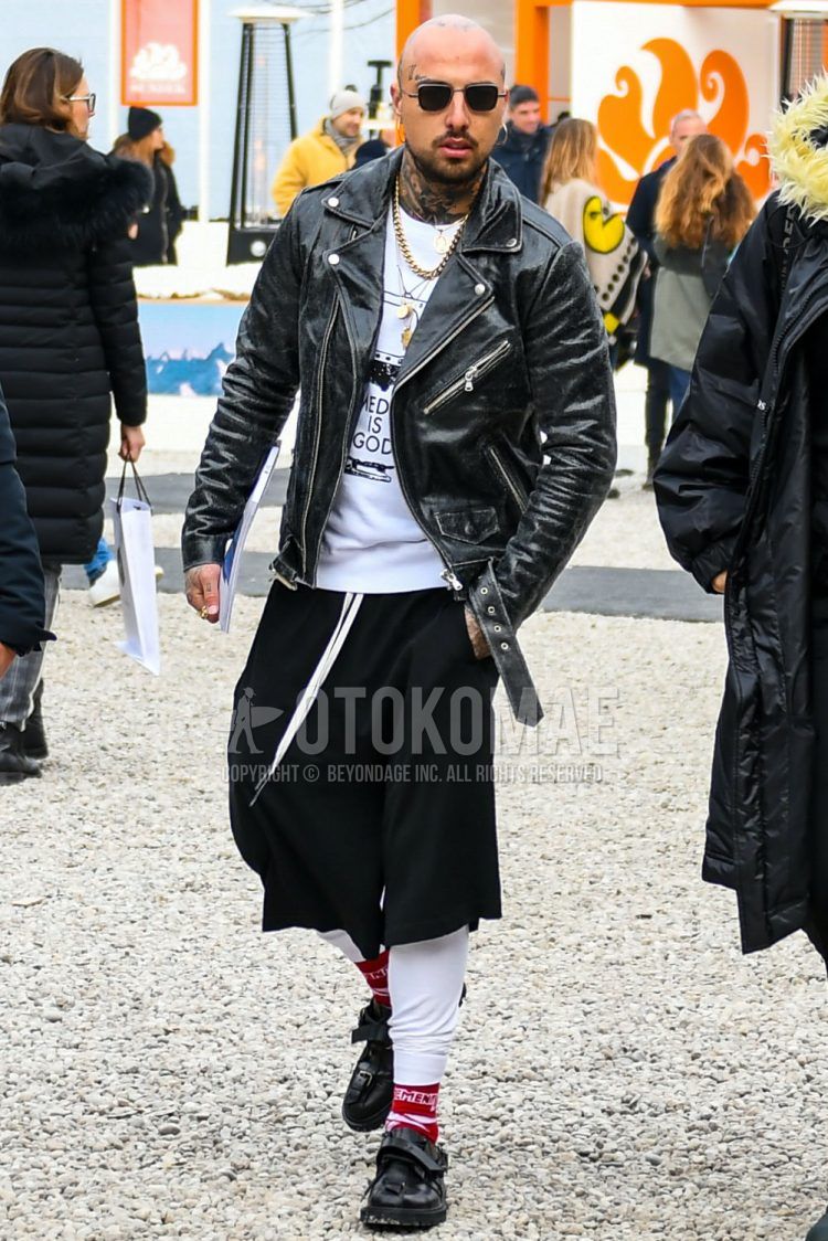 A men's fall/winter outfit with plain sunglasses, plain black rider's jacket, white graphic t-shirt, plain black sarouel pants, white other socks, and black monk shoe leather shoes.