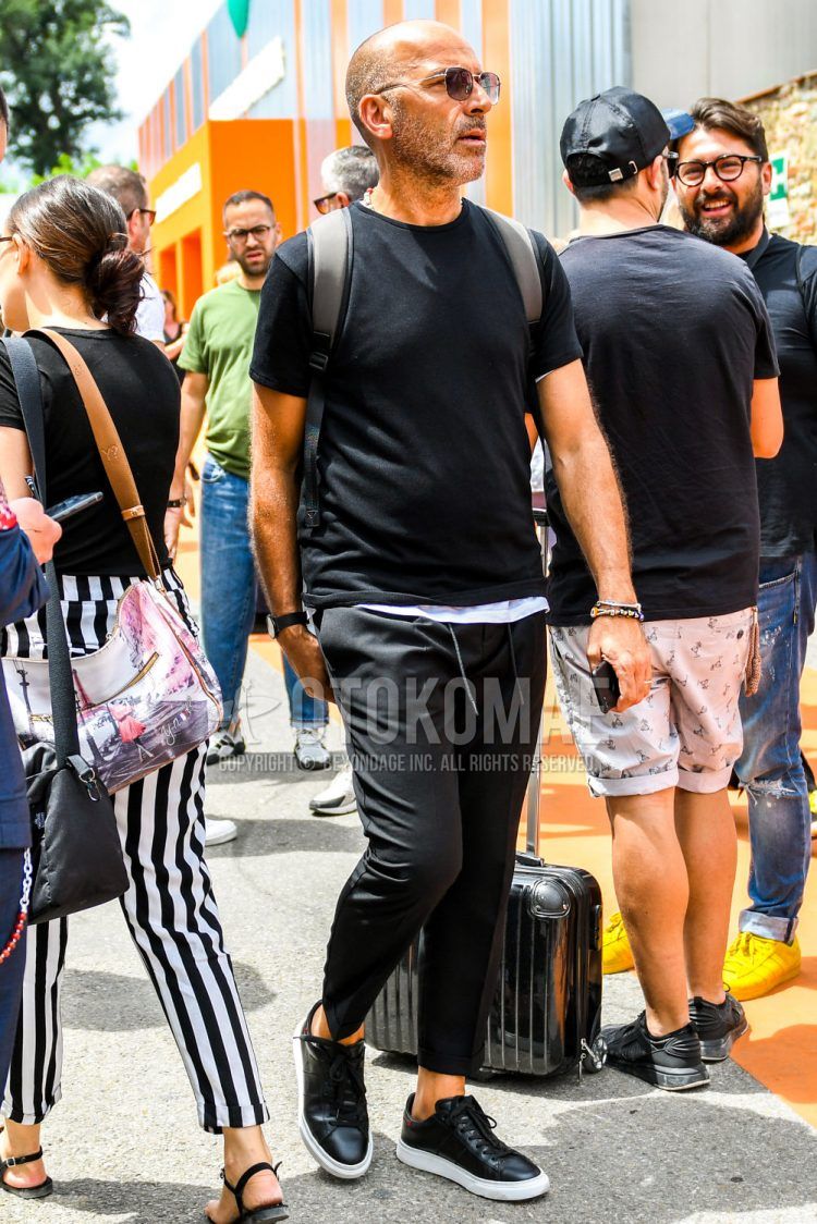 A summer men's coordinate outfit with plain sunglasses, a plain black t-shirt, plain black easy pants, and black low-cut sneakers.