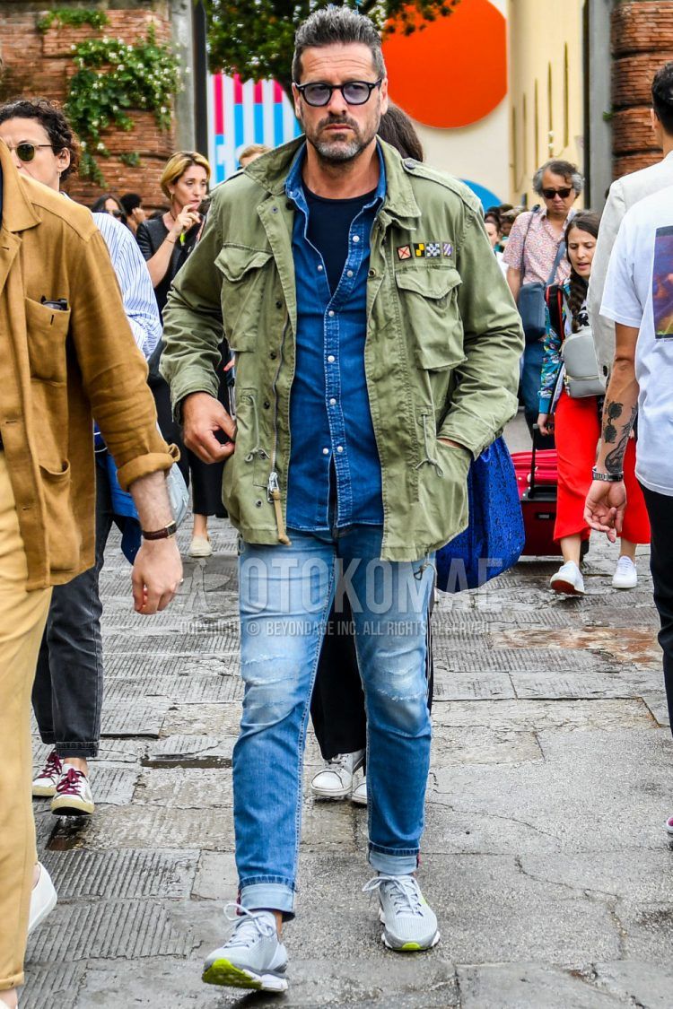 Spring/Summer/Fall men's coordinate outfit with solid black sunglasses, solid olive green M-65, solid blue denim/chambray shirt, solid navy t-shirt, solid blue denim/jeans, and gray low-cut sneakers.