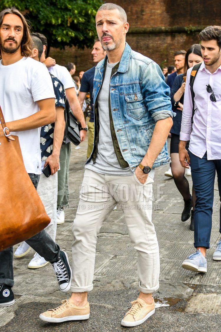 Spring/summer/fall men's coordinate outfit with plain blue denim jacket, plain olive green gilet, plain white t-shirt, plain white denim/jeans, and beige low-cut sneakers.