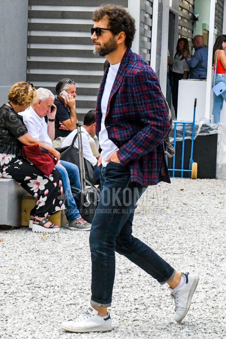 A men's fall/winter outfit with plain sunglasses, checked tailored jacket, plain white t-shirt, plain navy denim/jeans, and Adidas Stan Smith white low-cut sneakers.
