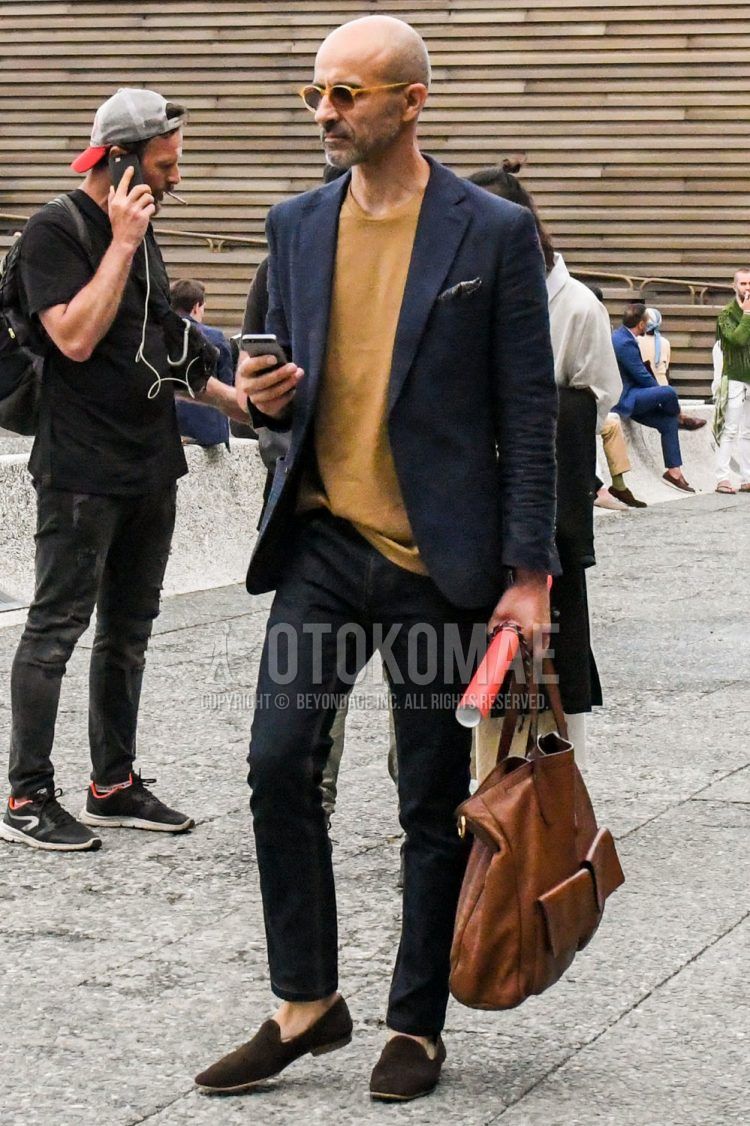 Solid color sunglasses, solid color navy tailored jacket, solid color yellow t-shirt, solid color navy denim/jeans, solid color navy ankle pants, brown suede shoes leather shoes, brown other loafer leather shoes, solid color brown tote bag, spring summer/fall men's outfits.