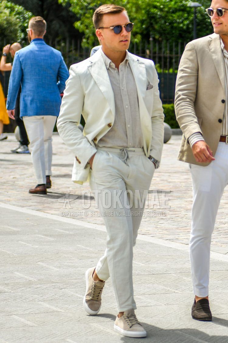 A men's spring/summer/fall outfit for men with plain sunglasses, plain white tailored jacket, plain beige shirt, plain white ankle pants, plain white easy pants, and beige low-cut sneakers.