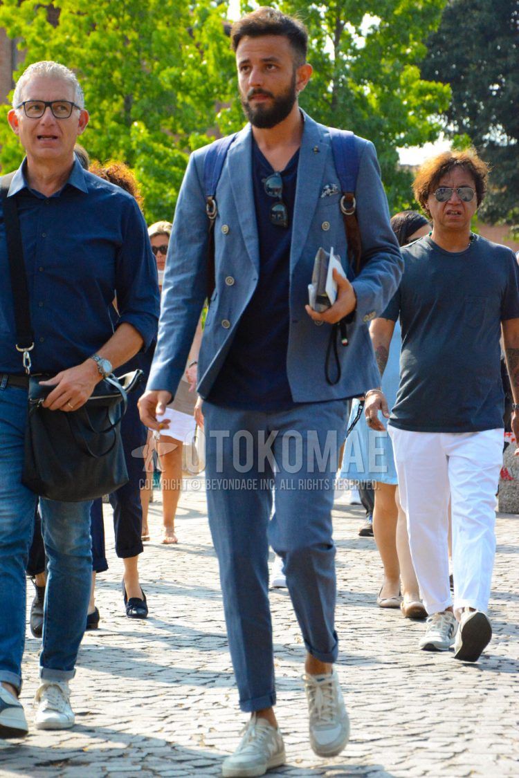 A men's spring/summer/fall outfit for men with plain sunglasses, a plain navy t-shirt, white low-cut sneakers, and a plain blue suit.