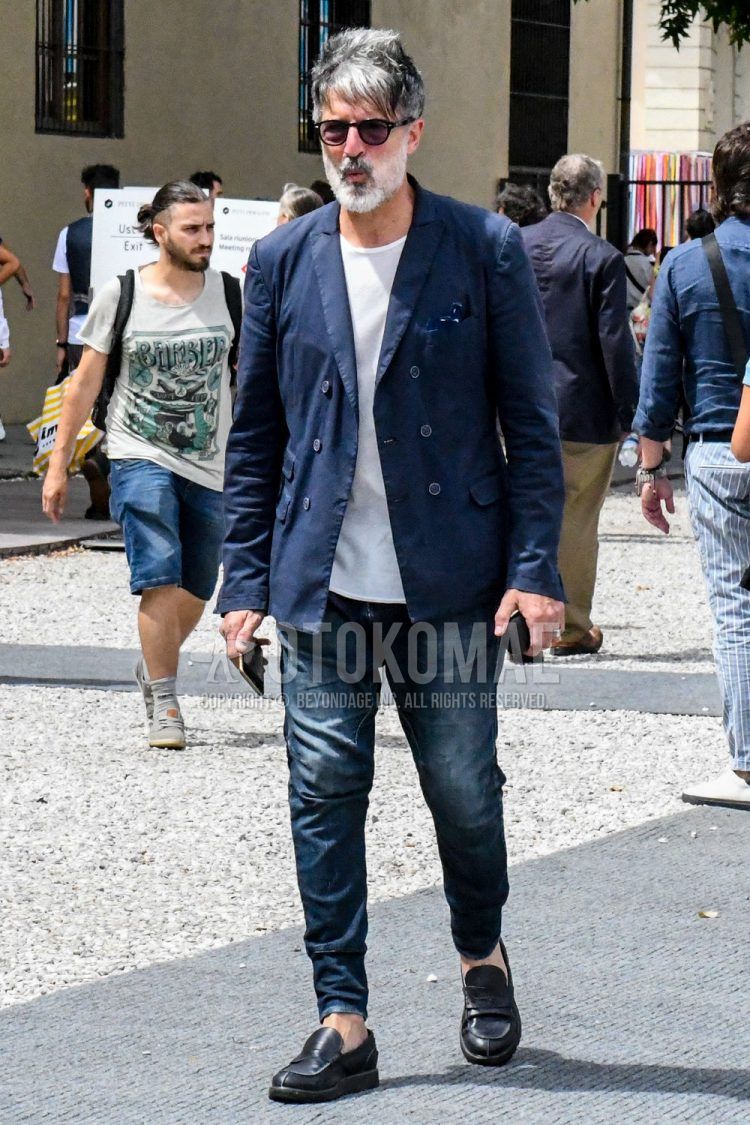 A summer/spring/fall men's coordinate outfit with a plain navy tailored jacket, plain white t-shirt, plain navy denim/jeans, and black coin loafer leather shoes.