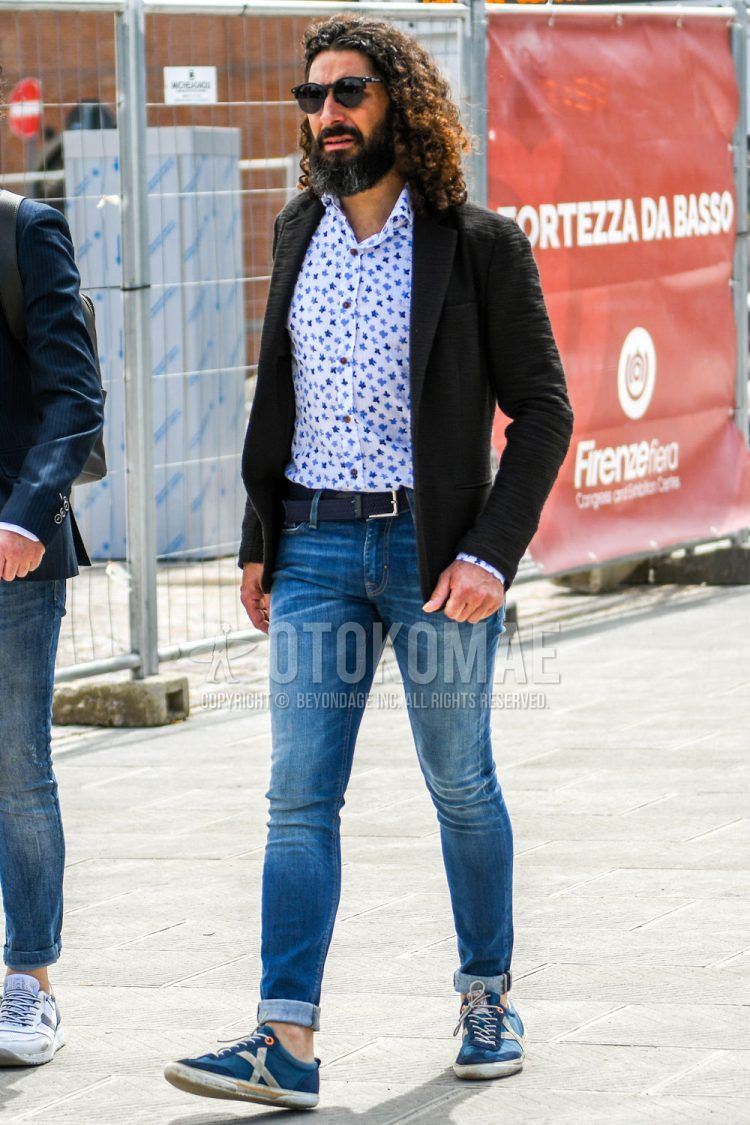 A spring/summer/fall men's coordinate outfit with solid color sunglasses, solid color black tailored jacket, white other shirt, solid color navy mesh belt, solid color blue denim/jeans, and blue low-cut sneakers.
