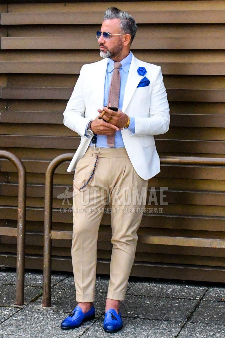 A men's spring/summer outfit with solid color sunglasses, solid color white tailored jacket, solid color light blue shirt, solid color beige slacks, solid color beige pleated pants, blue tassel loafer leather shoes, and solid color beige knit tie.