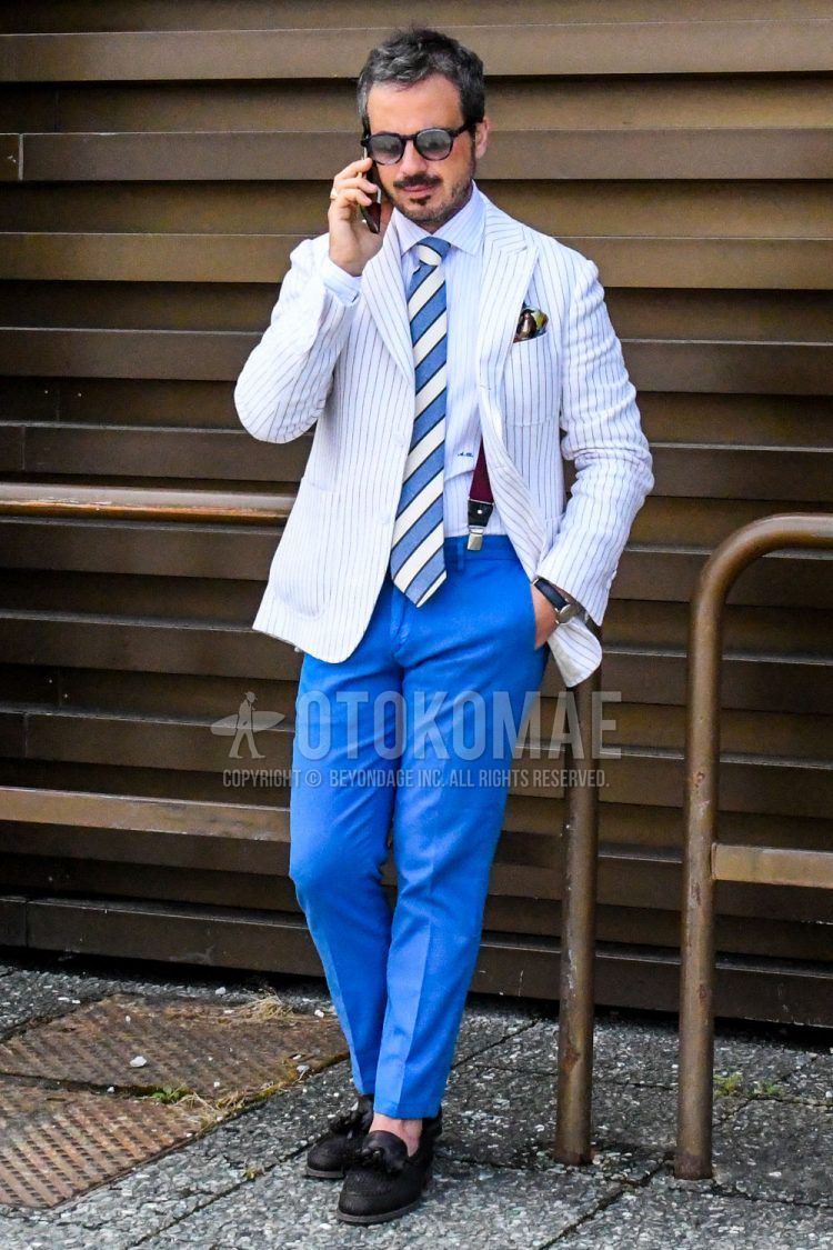 A summer-spring-fall men's outfit with solid color sunglasses, white striped tailored jacket, white striped shirt, solid color brown suspenders, solid color blue ankle pants, black tassel loafer leather shoes, and white/blue regimental tie.