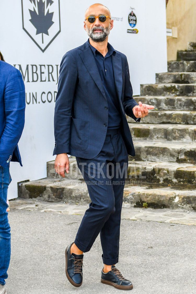 Spring, summer and fall men's coordinate outfit with plain orange sunglasses, plain navy polo shirt, navy low-cut sneakers and navy striped suit.