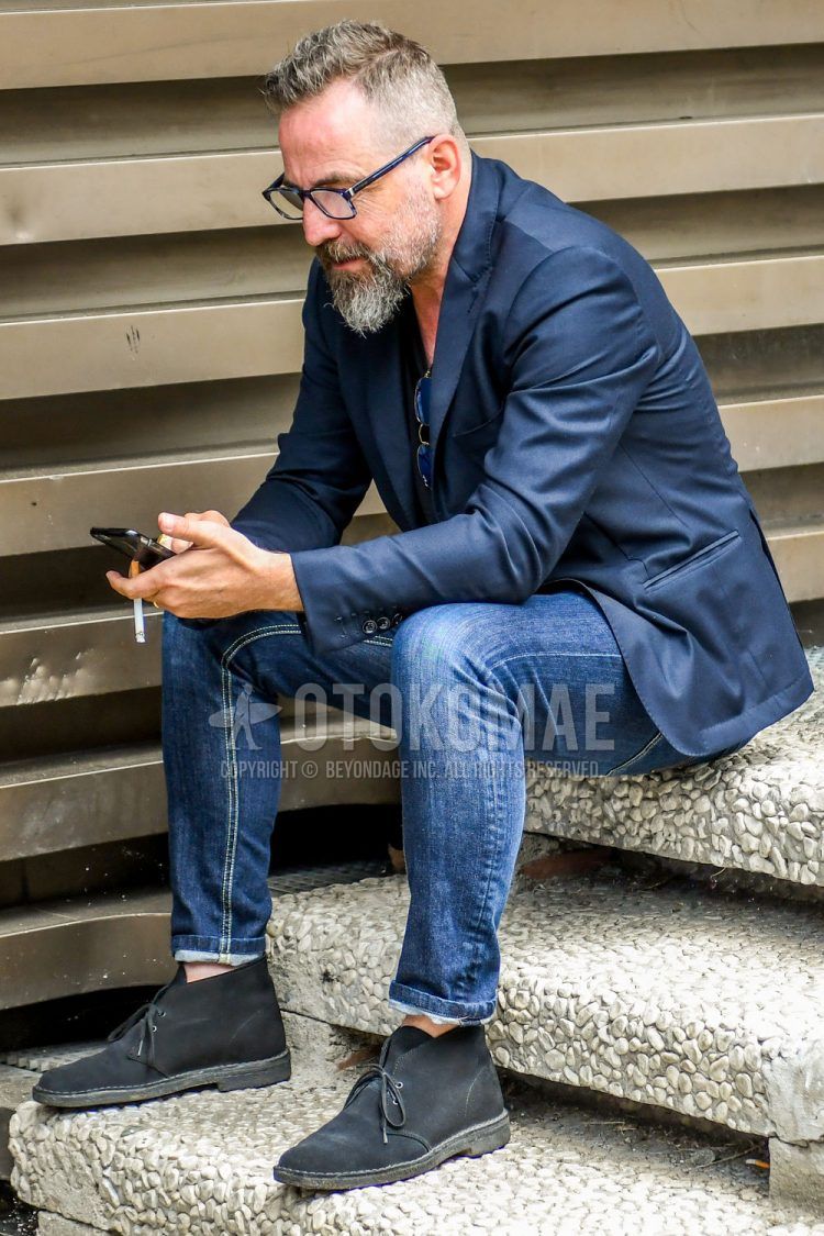 A spring/summer/fall men's coordinate outfit with plain glasses, plain navy tailored jacket, plain navy t-shirt, plain blue denim/jeans, and black chukka boots.