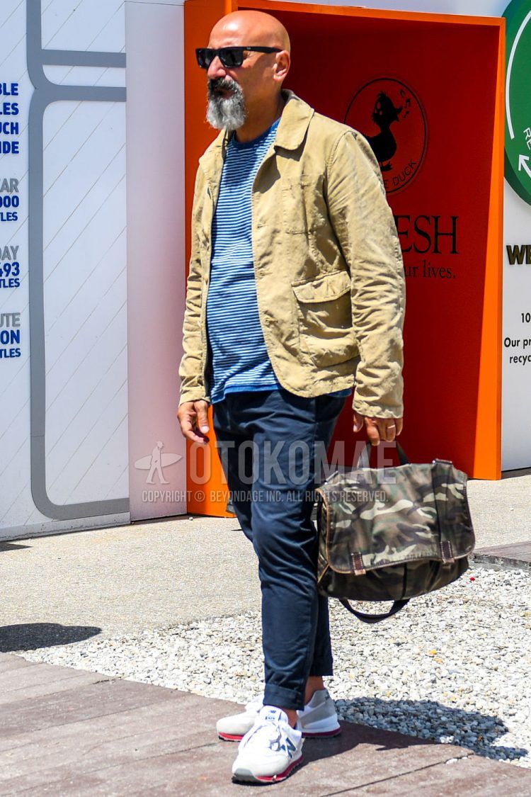 Spring, summer and fall men's coordinate outfit with solid color sunglasses, solid color others, blue/white striped t-shirt, solid color navy chinos, New Balance white low-cut sneakers and olive green camouflage shoulder bag.