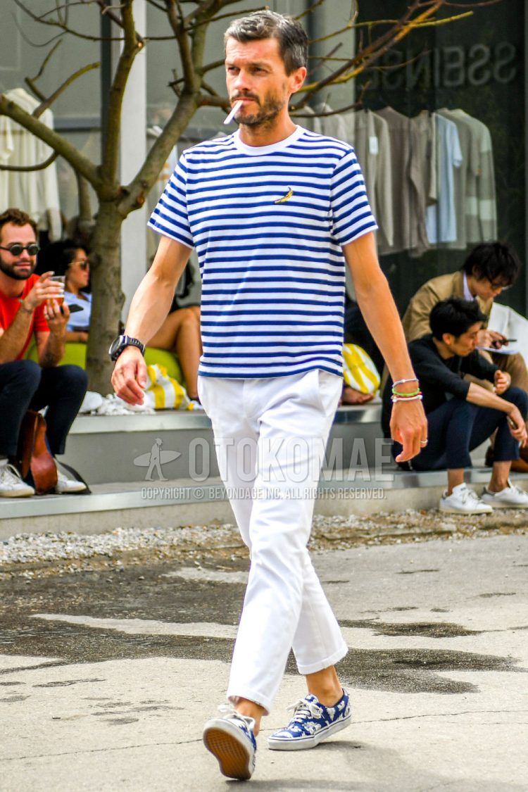 Summer men's coordinate outfit with blue/white striped t-shirt, plain white ankle pants, plain white cotton pants, and blue low-cut sneakers from Vans.