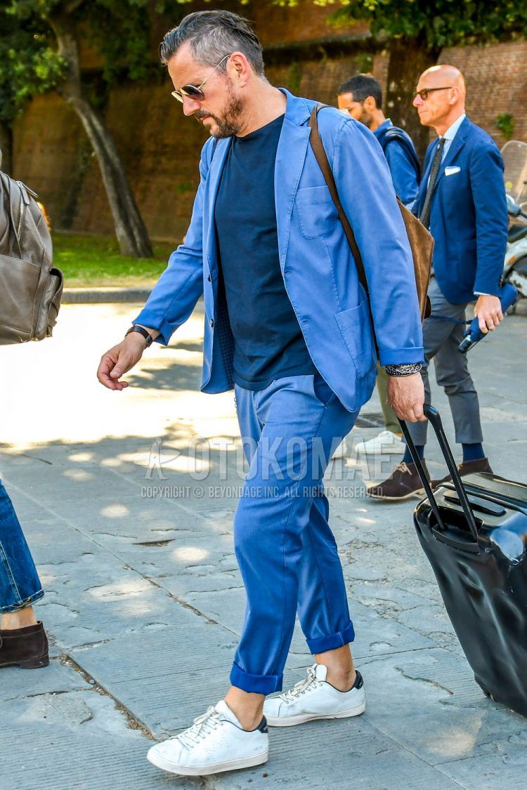 A men's spring/summer/fall outfit for men with plain sunglasses, plain navy t-shirt, white low-cut sneakers, other solid colors, and a solid blue suit.