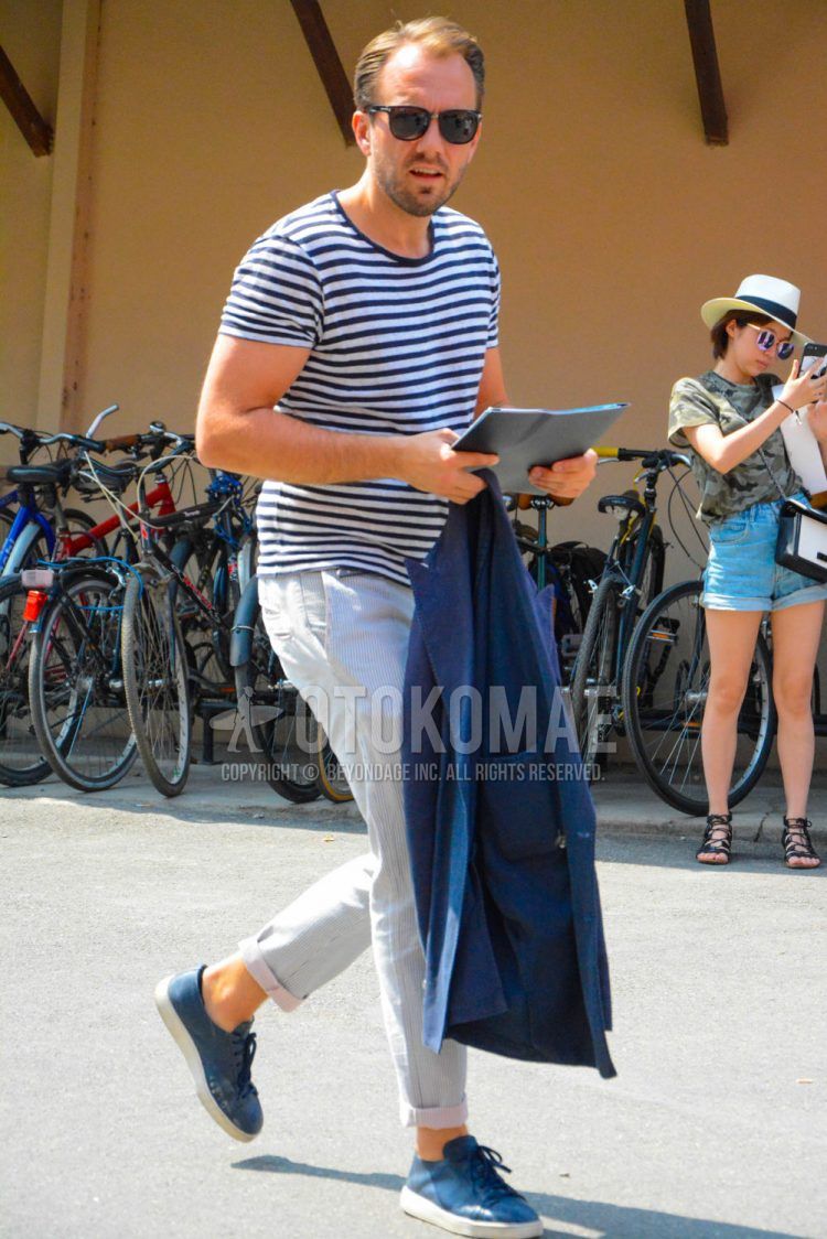 A men's spring/summer coordinate outfit with plain sunglasses, a black/white striped t-shirt, plain white cotton pants, and blue low-cut sneakers.