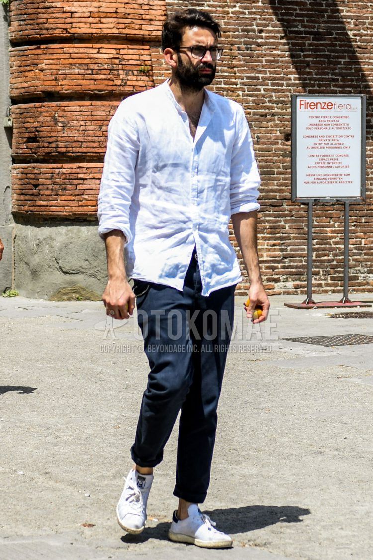 A summer/spring men's coordinate outfit with plain glasses, plain white shirt, plain navy chinos, and Adidas Stan Smith white low-cut sneakers.