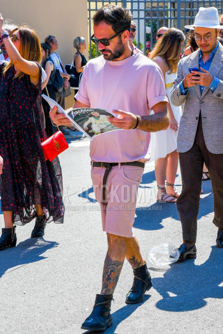 A summer men's coordinate outfit with plain sunglasses, a plain pink t-shirt, a plain black leather belt, plain pink shorts, and black other boots.