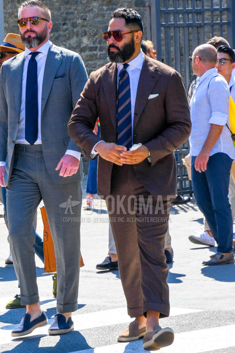 A men's spring/summer/fall outfit with plain sunglasses, plain white shirt, plain beige espadrilles, plain brown suit, and navy regimental tie.