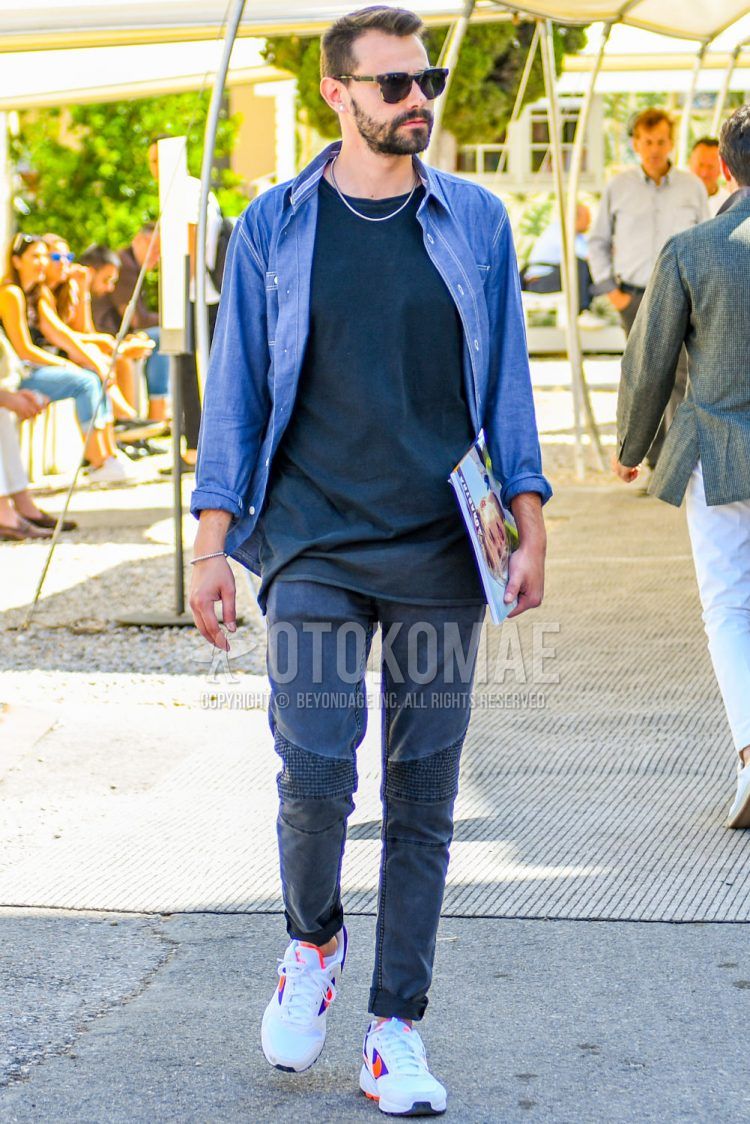 A spring/summer men's coordinate outfit with solid color sunglasses, solid color blue shirt, solid color navy t-shirt, solid color gray damaged jeans, and white low-cut Nike sneakers.
