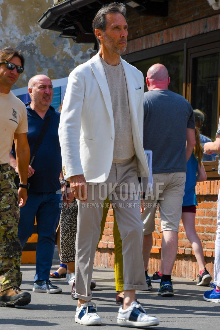 Spring, summer and fall men's coordinate outfit with plain white tailored jacket, plain beige t-shirt, plain beige chinos and Valentino white low-cut sneakers.