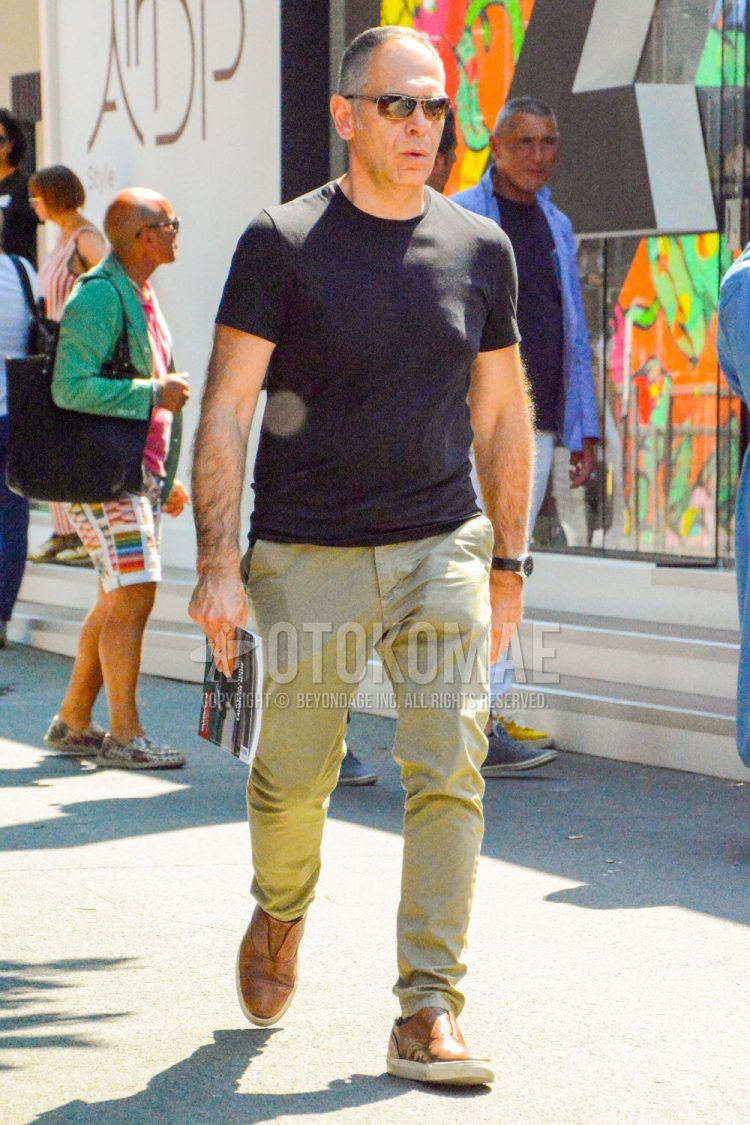 A spring/summer men's coordinate outfit with plain sunglasses, a plain black T-shirt, plain beige chinos, and brown slip-on sneakers.