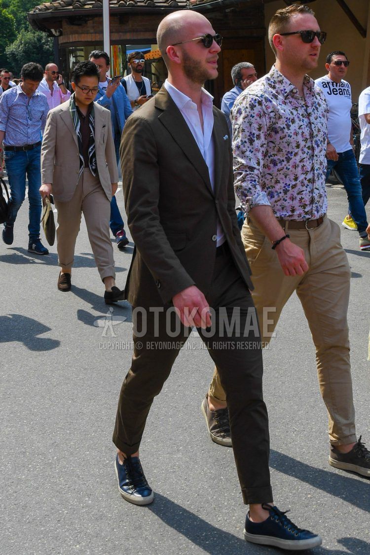 A spring/summer/fall men's coordinate outfit with plain sunglasses, a plain white shirt, black/navy low-cut sneakers, and a plain brown suit.