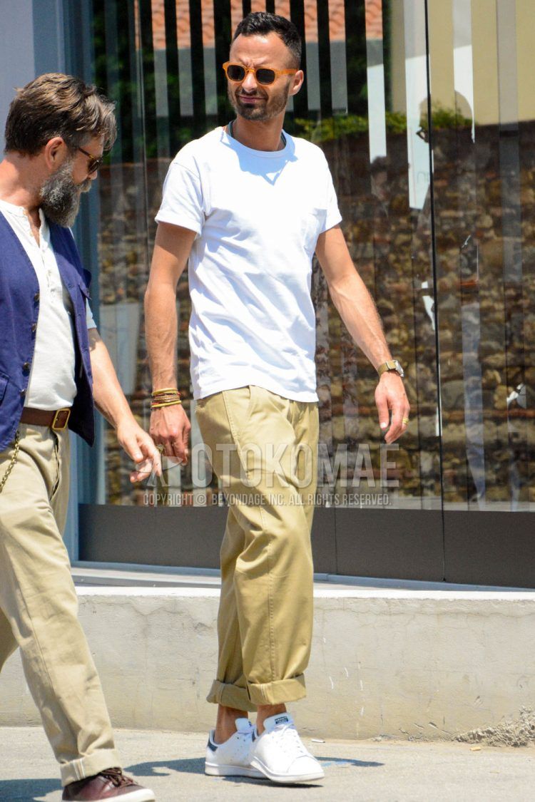 A summer men's coordinate outfit with plain sunglasses, a plain white t-shirt, plain beige chinos, and white low-cut Adidas sneakers.